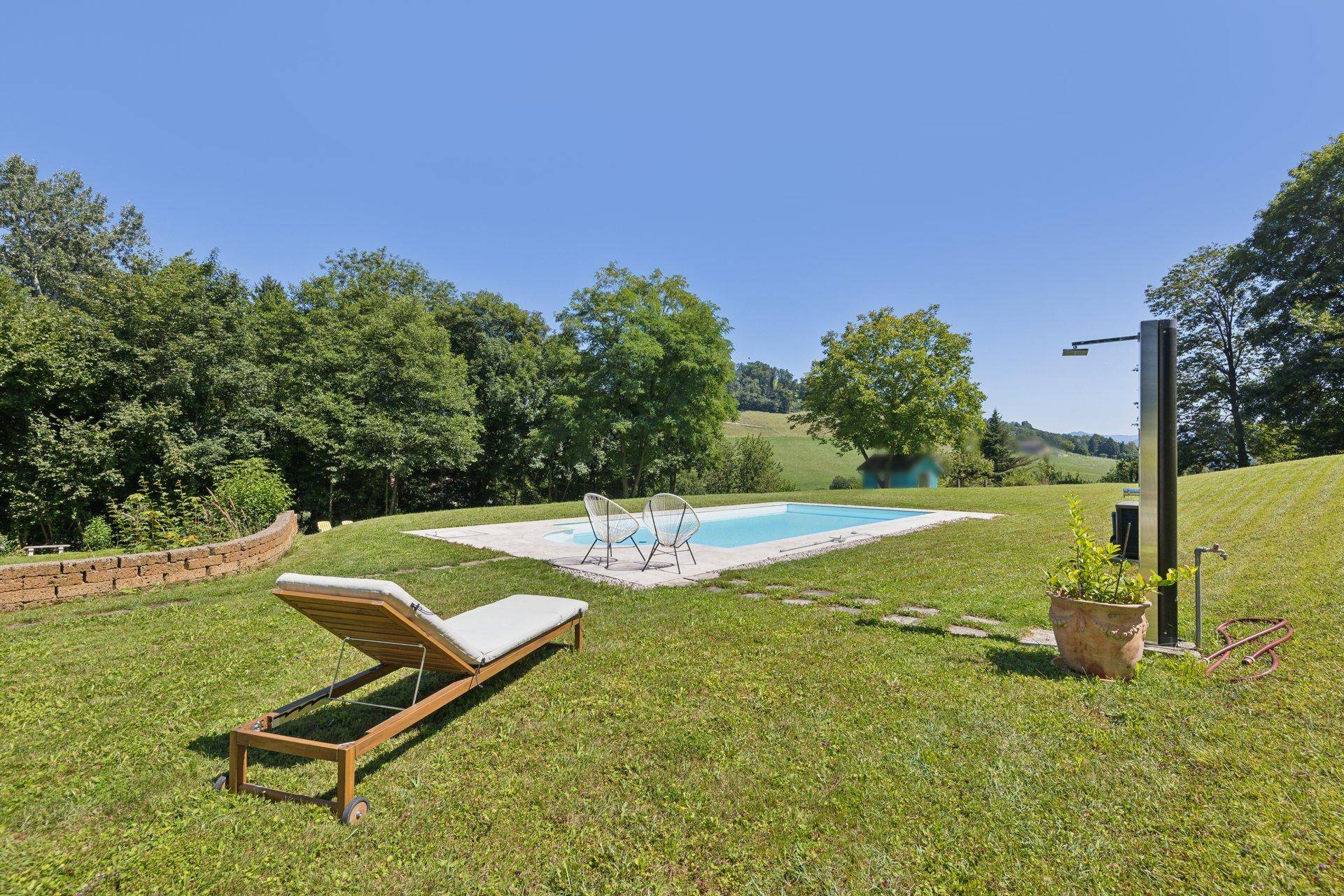 Idyllischer Garten mit Pool, Liegestühlen und Außendusche, umgeben von Natur.