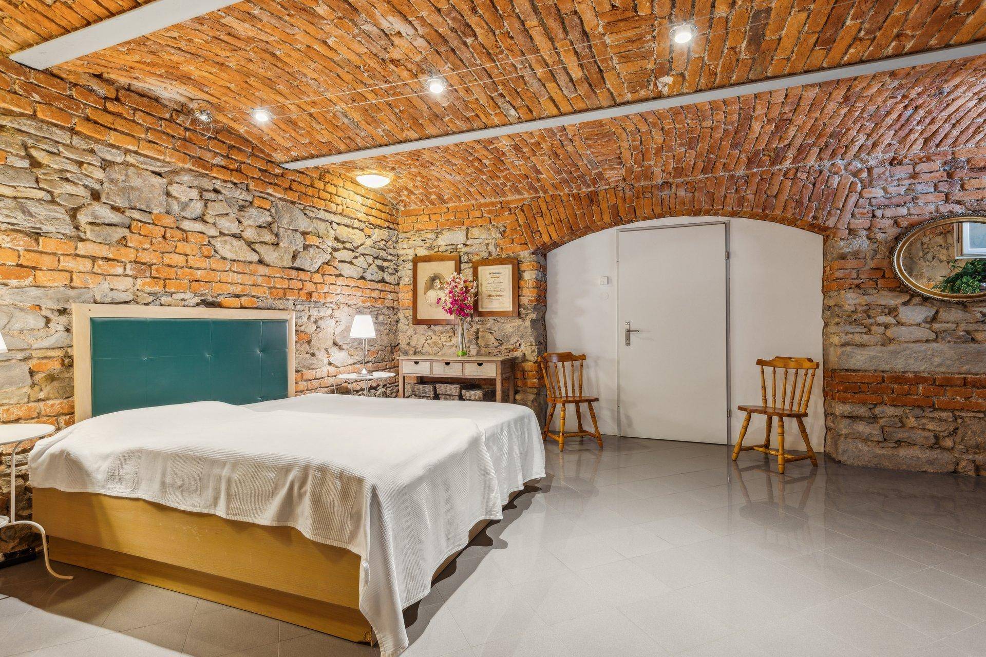 Rustikales Schlafzimmer mit freigelegten Ziegelwänden und Gewölbedecke, modern gefliestem Boden.