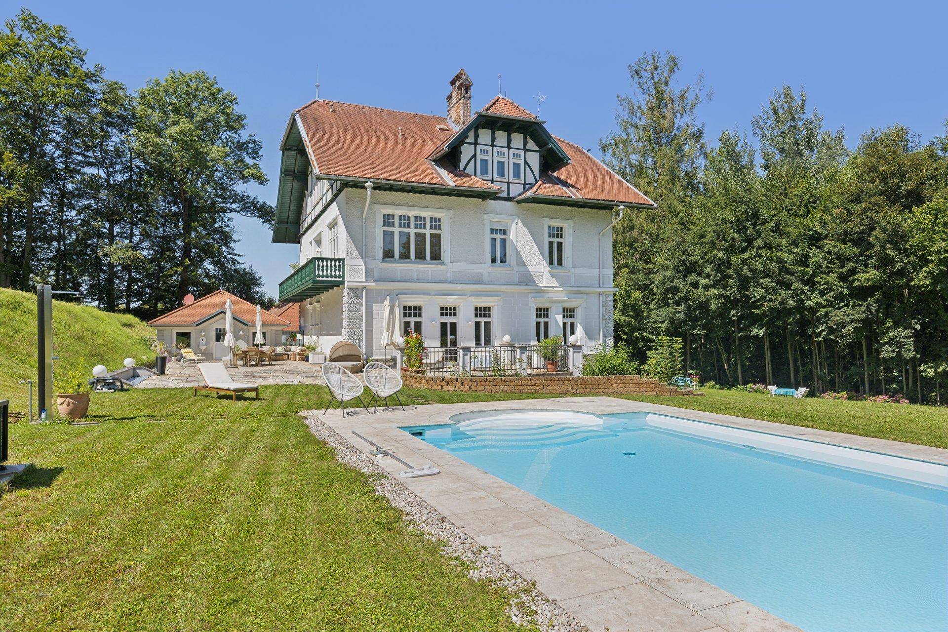 Elegante Villa mit großem Pool und weitläufigem Garten, umgeben von grüner Landschaft.