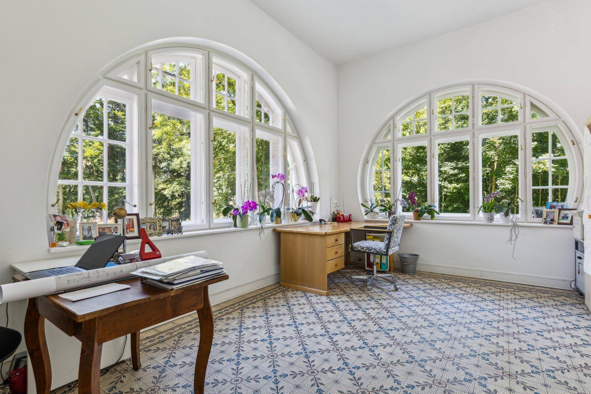 Arbeitszimmer mit einzigartigen Rundbogenfenstern und gemustertem Fliesenboden, umgeben von Grün.