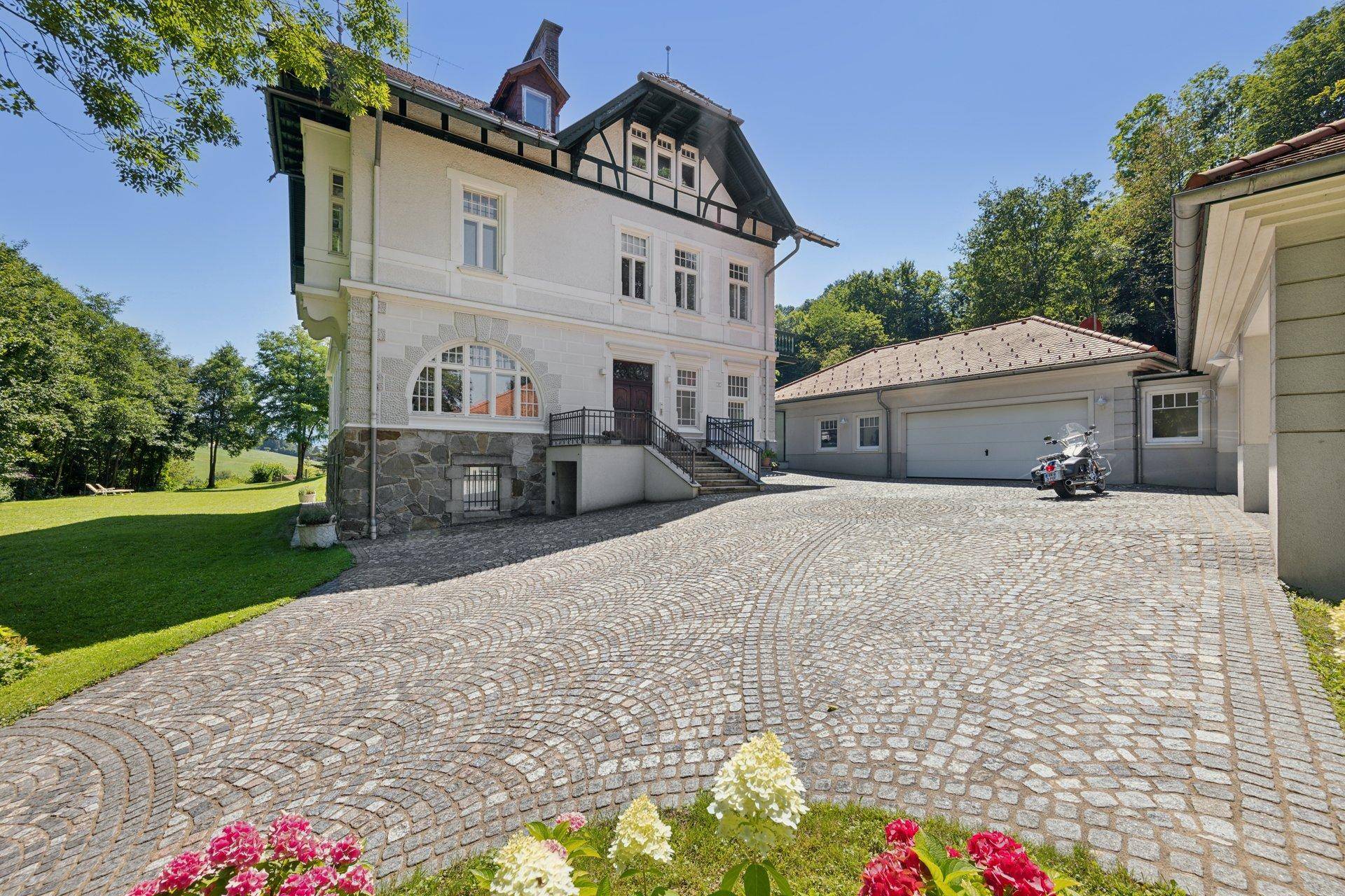 Herrschaftliche Villa mit gepflasterter Auffahrt und separatem Garagengebäude.