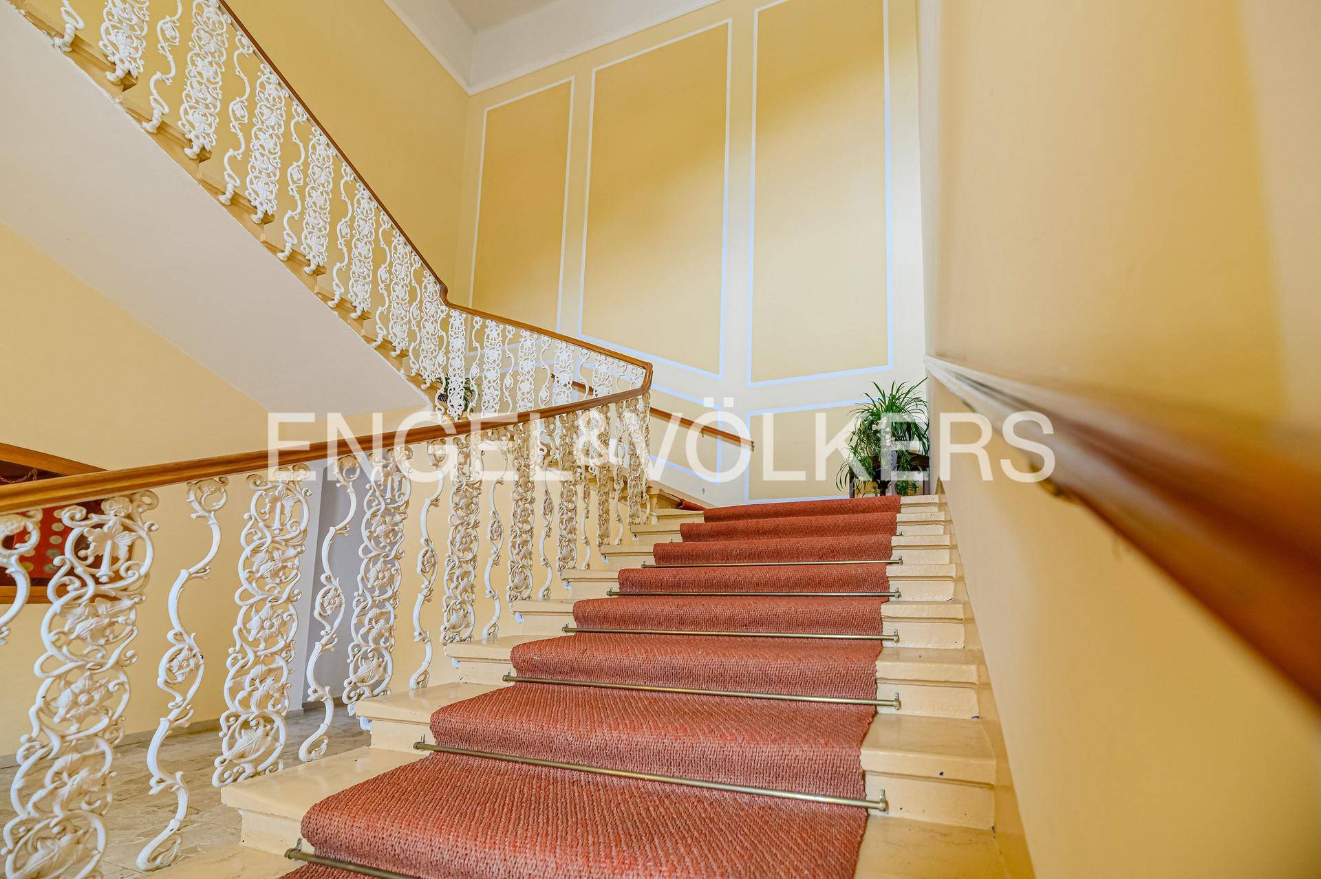 Elegantes Treppenhaus mit schmiedeeisernem Geländer, Teppichläufer und hohen Wänden.