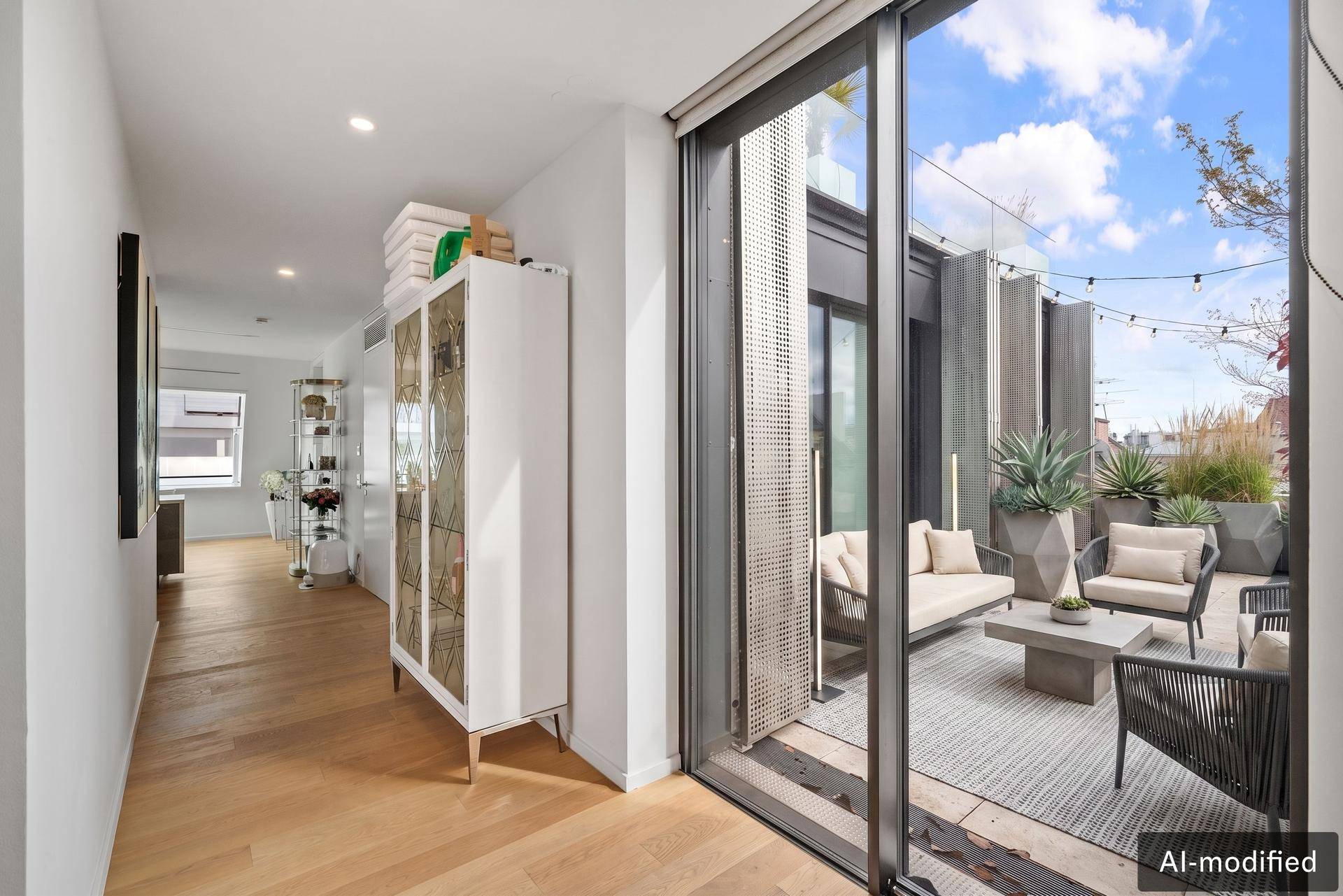 Moderner Flur mit Holzboden und großem Schiebefenster, das zur möblierten Terrasse führt.