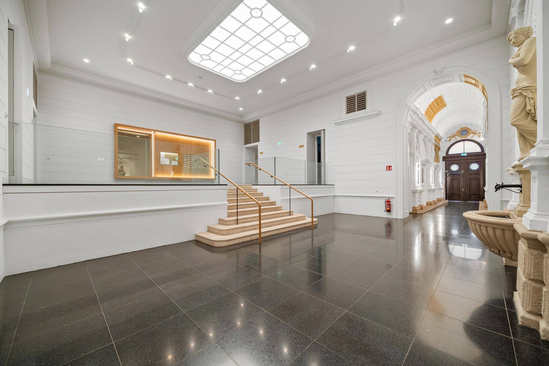 Prunkvolle Eingangshalle mit hohen Decken, dunklem Fliesenboden und einer eleganten Treppe.