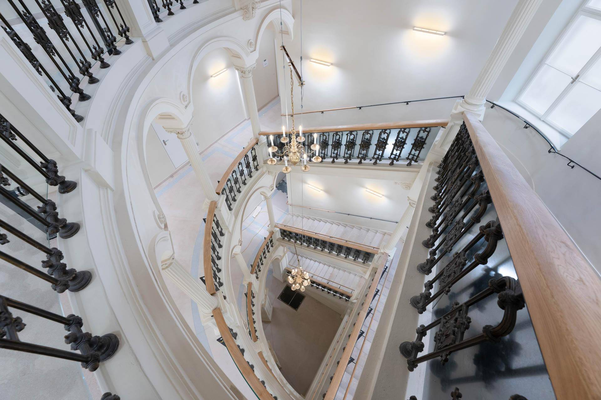 Elegantes Treppenhaus mit kunstvollem Geländer, hohen Decken und Kronleuchtern.