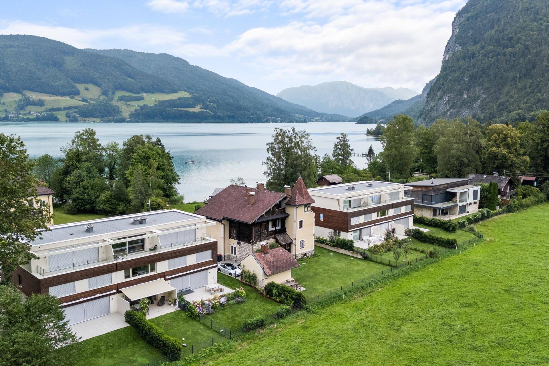 Panoramablick auf moderne Gebäude und ein traditionelles Haus am Seeufer mit Bergblick.