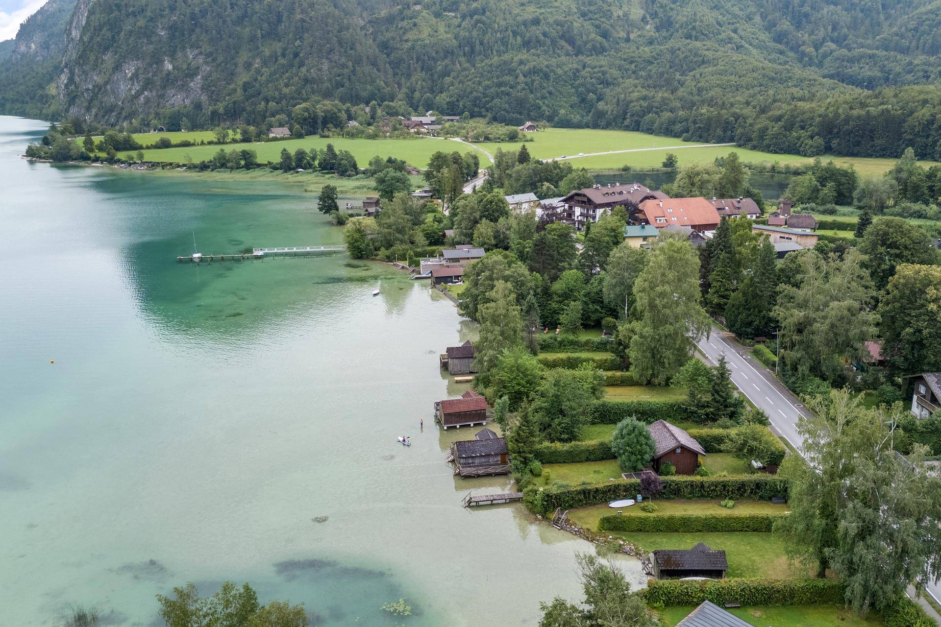 Luftaufnahme einer malerischen Seenlandschaft mit Häusern am Ufer und grünen Bergen.