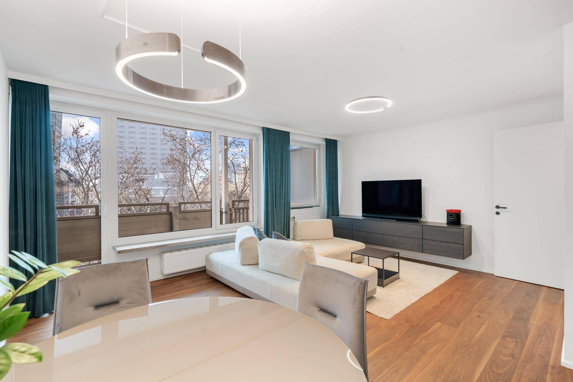 Moderner Wohnbereich mit großem Sofa, Fernseher und Esstisch, hell und offen gestaltet.