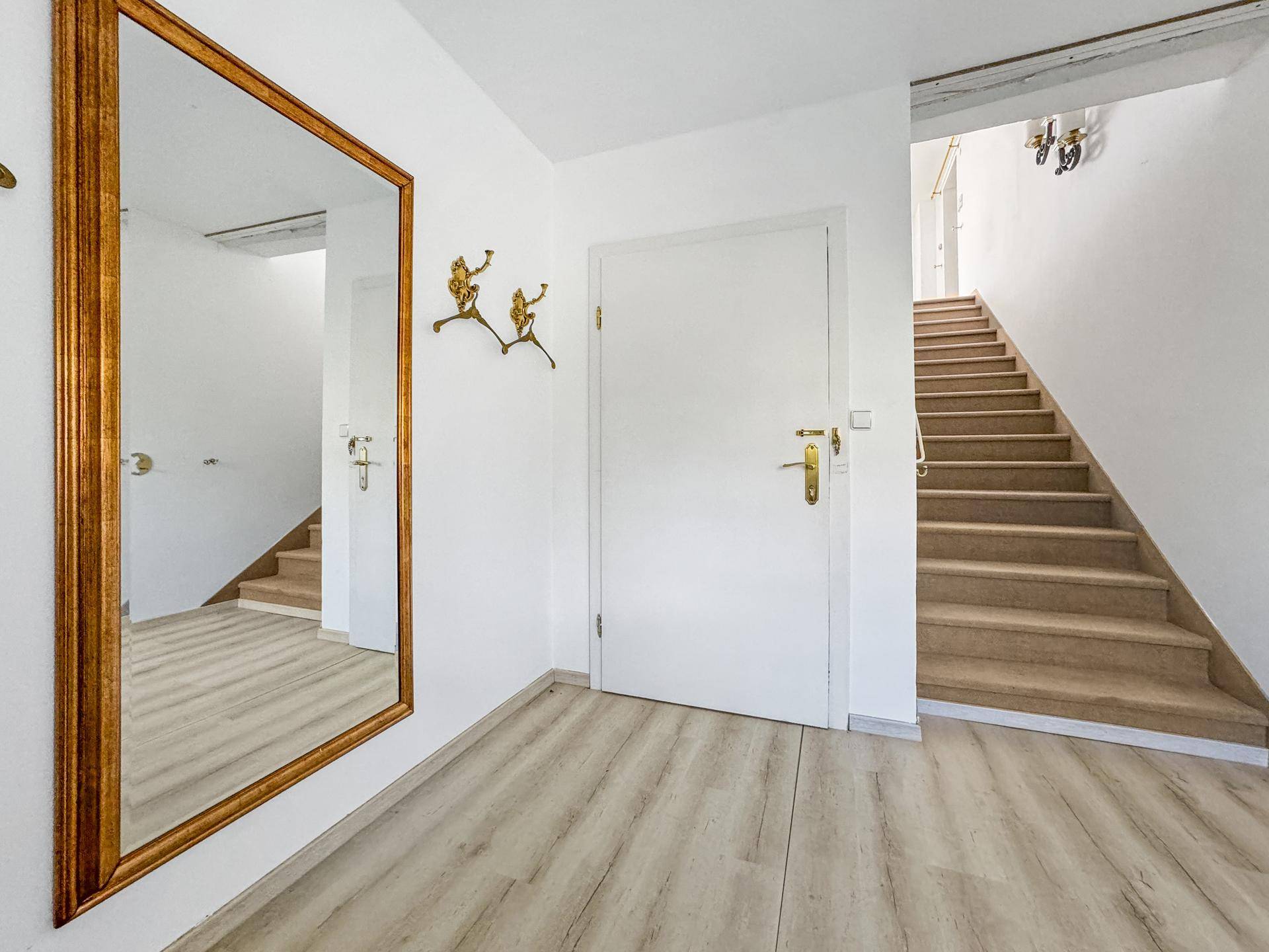 Heller Flur mit Holzoptik-Boden, großem Spiegel und Treppe zum Obergeschoss.