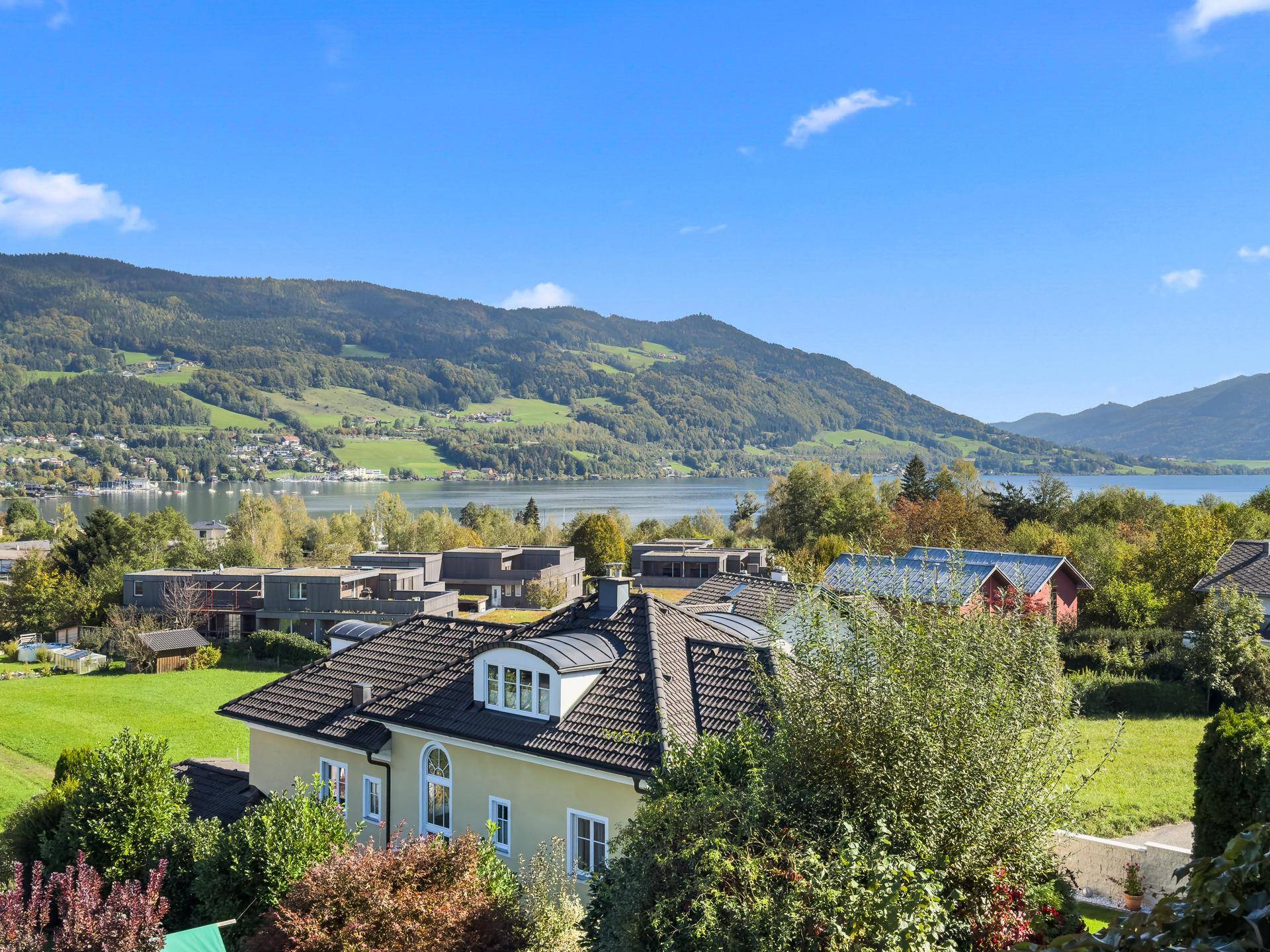 Panoramablick auf ein Wohnhaus mit See- und Bergblick, umgeben von grüner Landschaft.