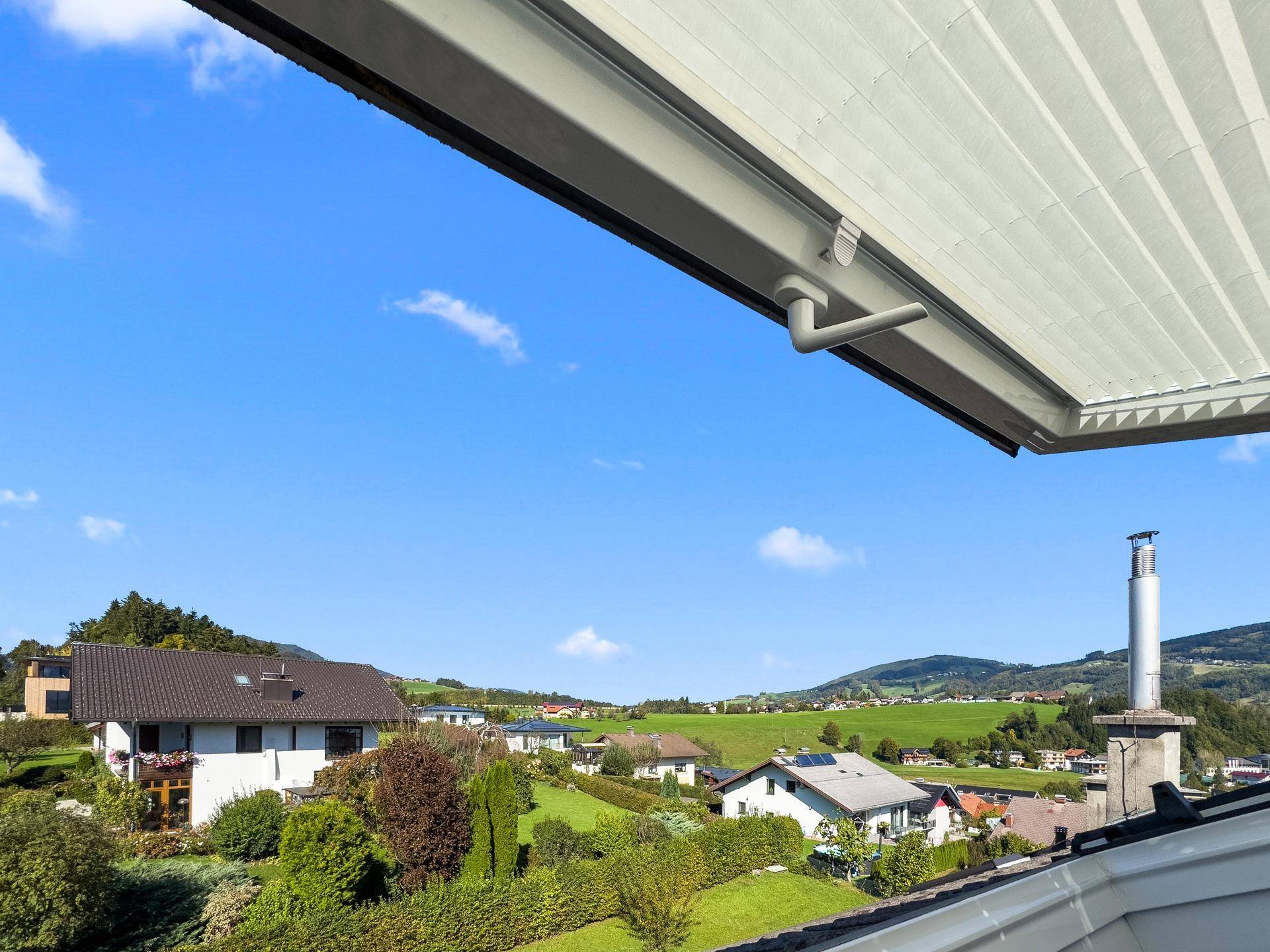 Weitläufiger Blick über die grüne Hügellandschaft mit verstreuten Häusern unter blauem Himmel.
