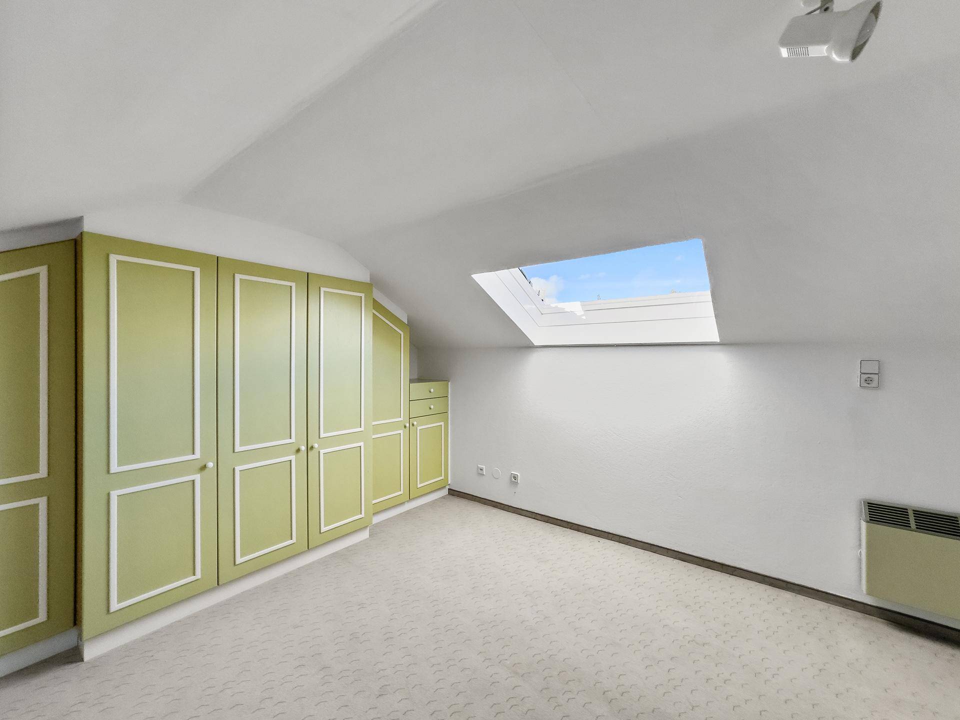 Schlafzimmer mit Dachschräge, Einbauschränken in Hellgrün und einem Dachfenster.