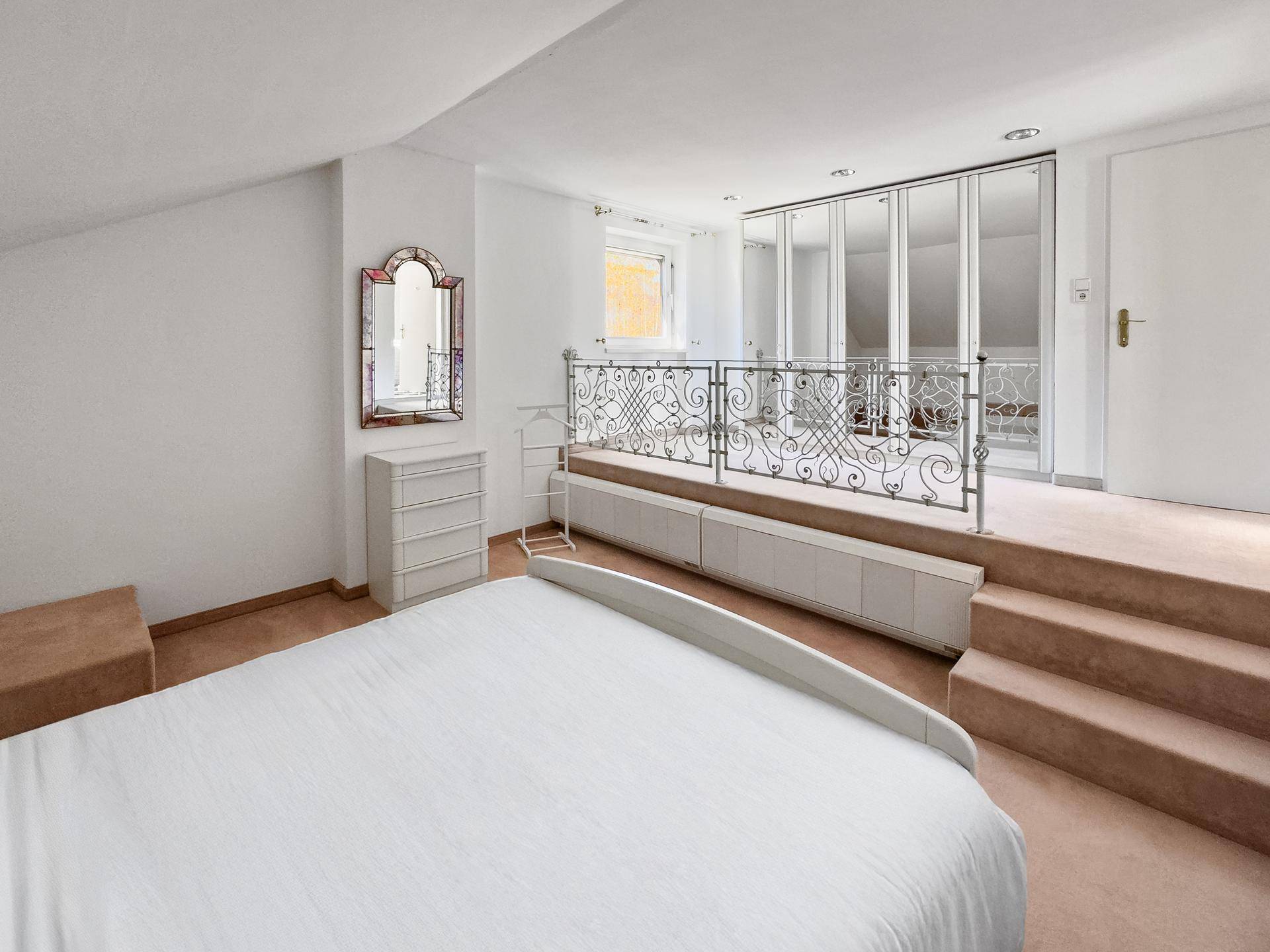 Gemütliches Schlafzimmer mit Teppichboden, Dachschräge und einem erhöhten Bereich mit Spiegelkleiderschrank.