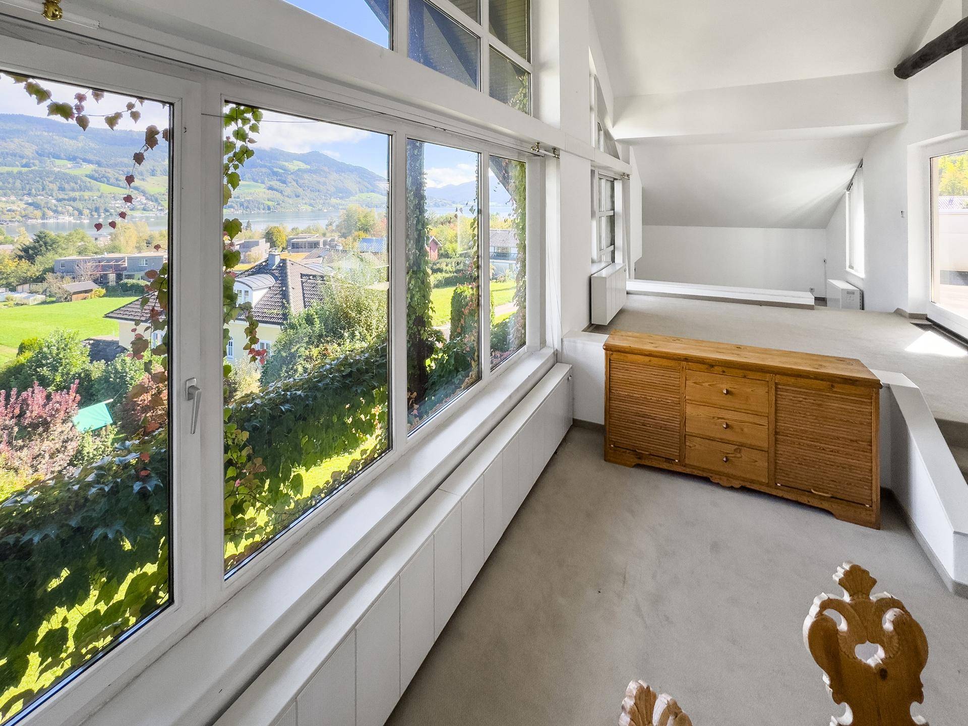 Heller Wohnbereich mit großen Fenstern und Blick auf die grüne Landschaft, ausgestattet mit Holzmöbeln.