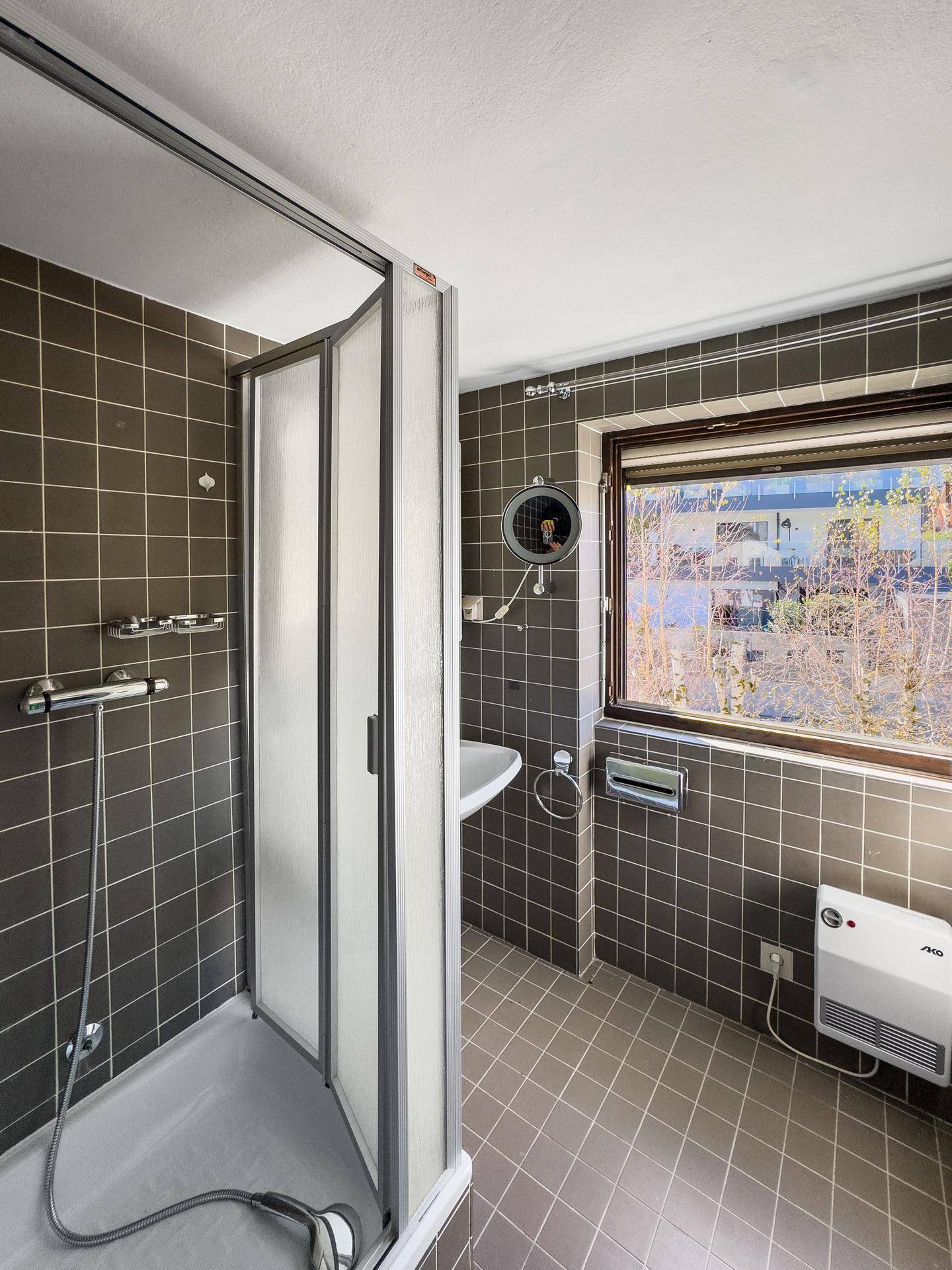 Badezimmer mit braunen Fliesen, Duschkabine und Fenster für natürliche Belüftung.