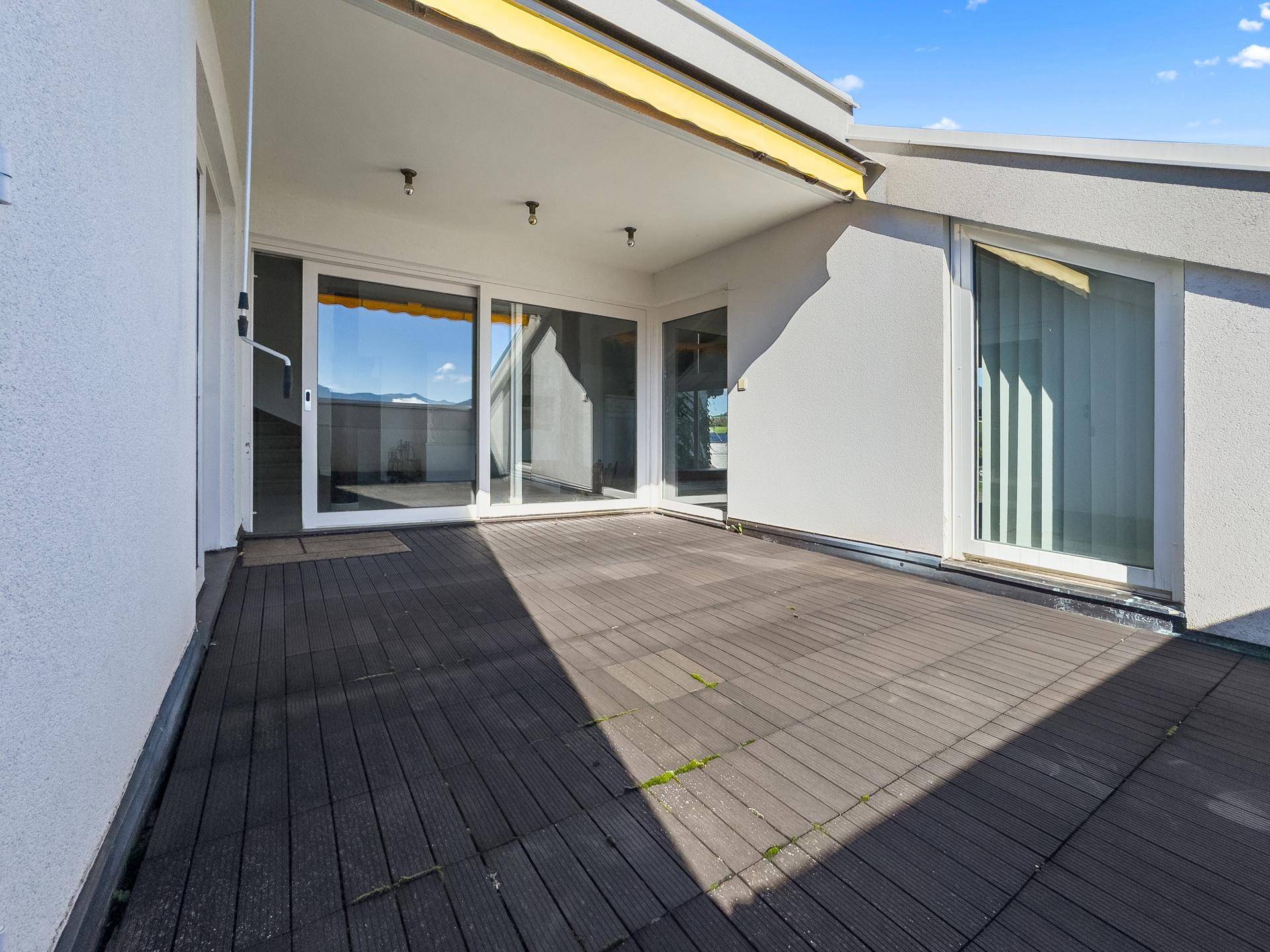 Geräumige Dachterrasse mit Holzboden und Schiebetüren, ideal für Entspannung im Freien.