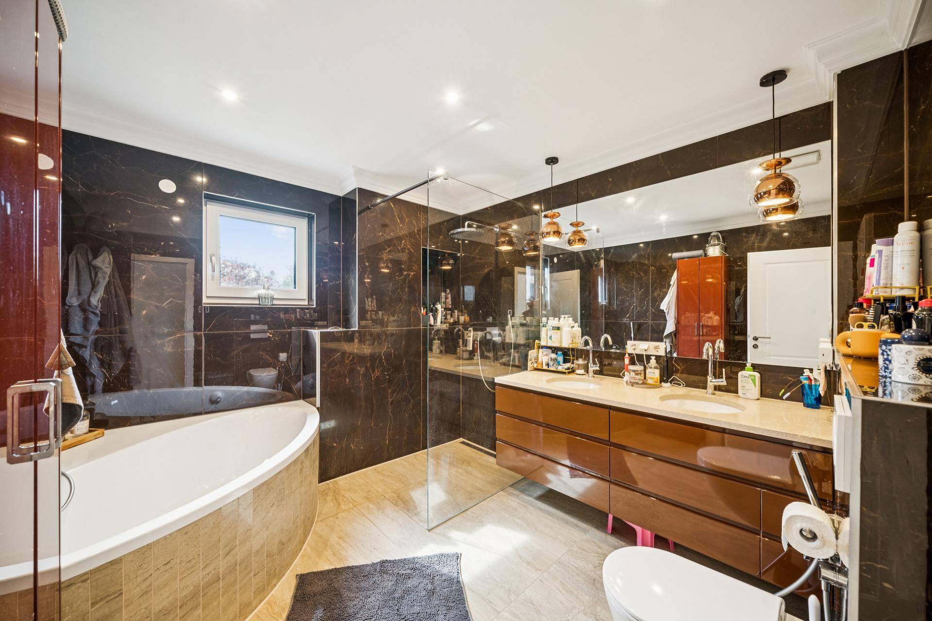 Luxuriöses Badezimmer mit dunklen Marmorfliesen, großer Badewanne und begehbarer Dusche.
