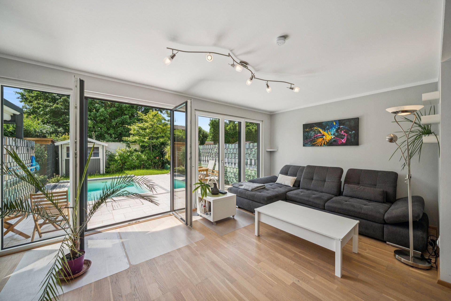 Helles Wohnzimmer mit modernem Sofa, Holzboden und direktem Zugang zum Garten mit Pool.