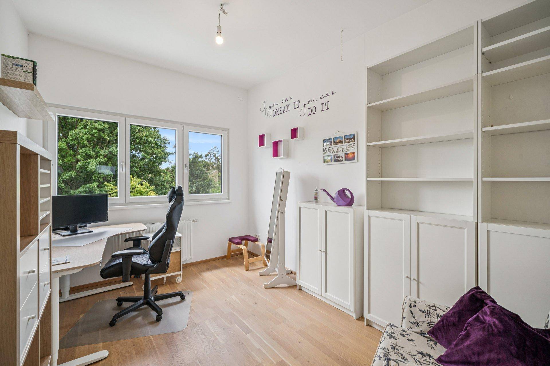 Funktionales Arbeitszimmer mit Schreibtisch, Bücherregalen und Blick ins Grüne durch das große Fenster.