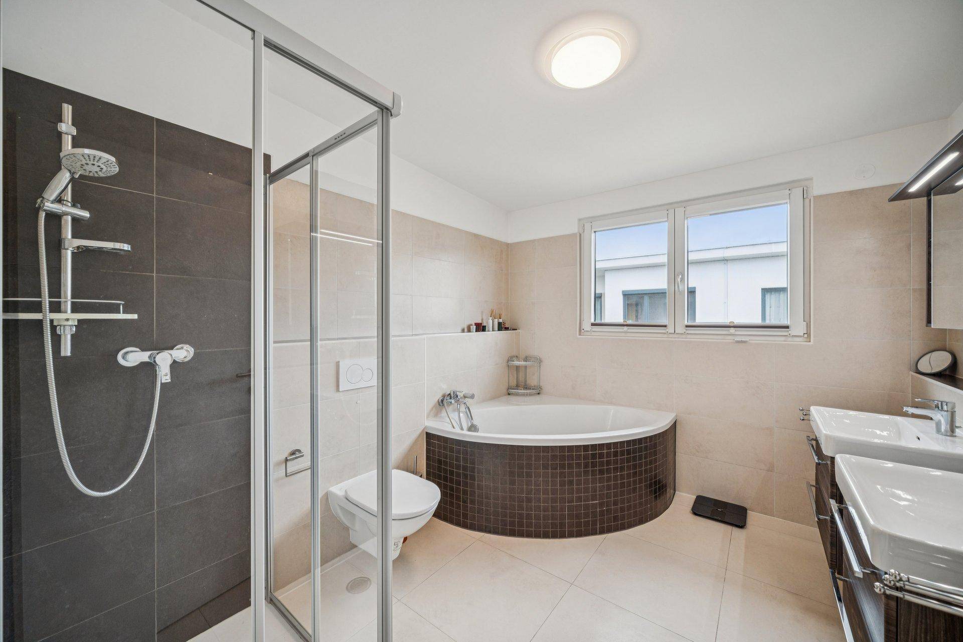 Modernes Badezimmer mit Dusche, Eckbadewanne, Doppelwaschbecken und einem Fenster für Tageslicht.