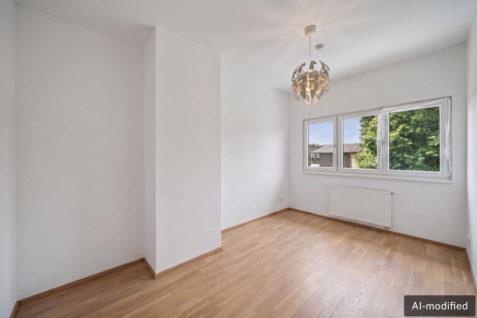 Helles Zimmer mit Holzboden, weißen Wänden und großem Fenster, ideal als Schlaf- oder Arbeitszimmer.