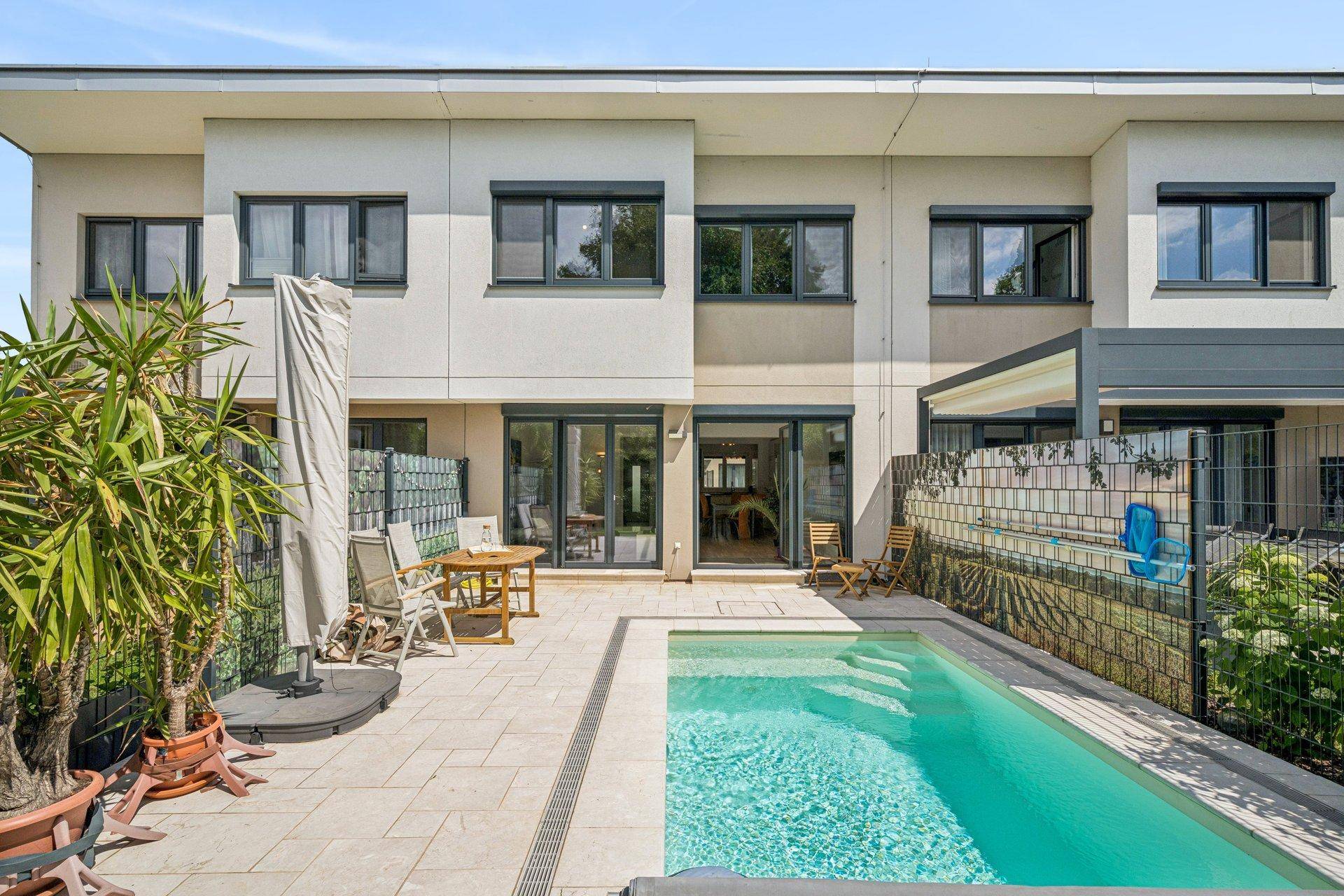 Rückansicht des Hauses mit privatem Pool, gepflasterter Terrasse und Sitzgelegenheiten unter einer Pergola.
