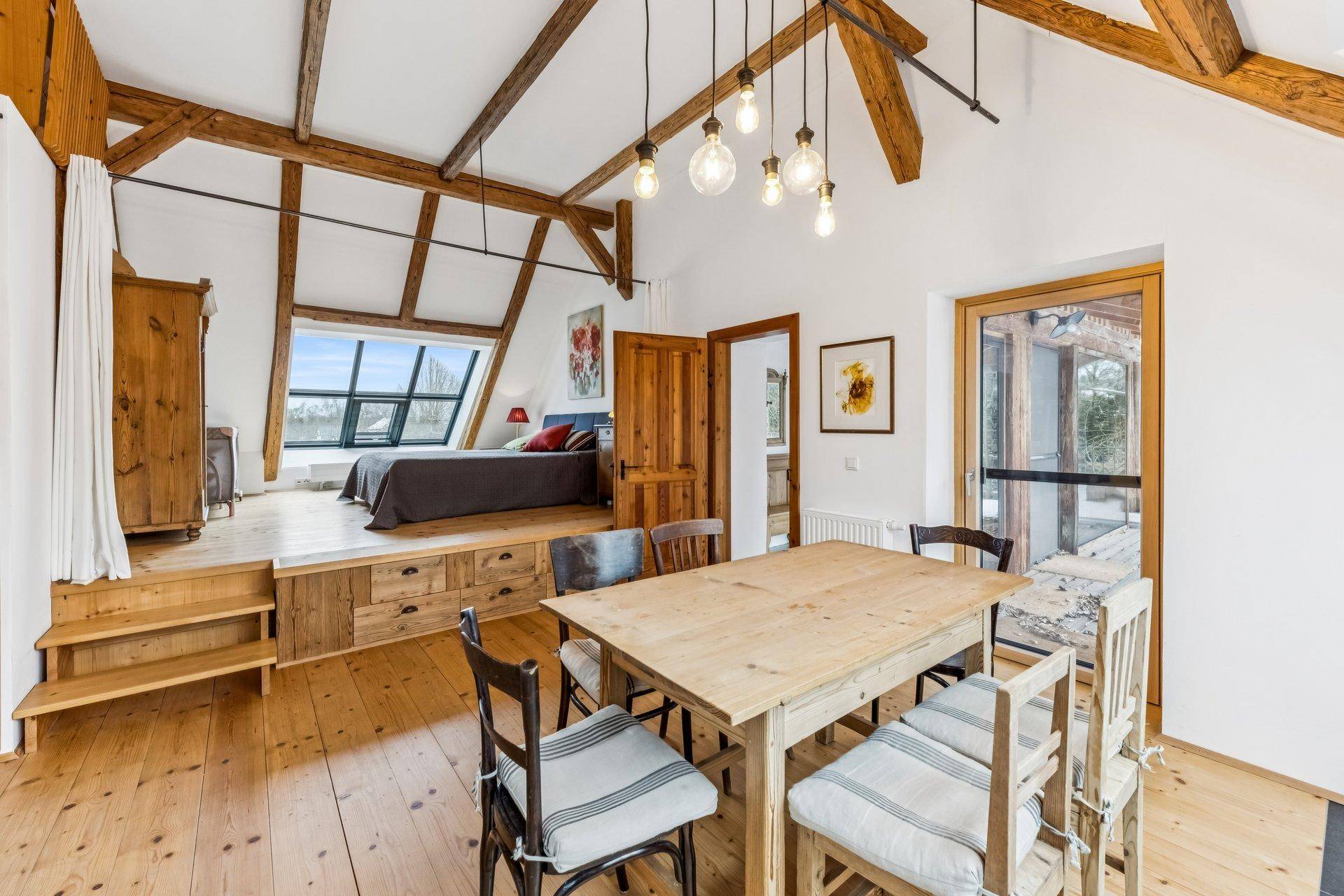 Offenes Schlafzimmer mit Holzbalken, Essbereich und großen Dachfenstern für viel Licht.