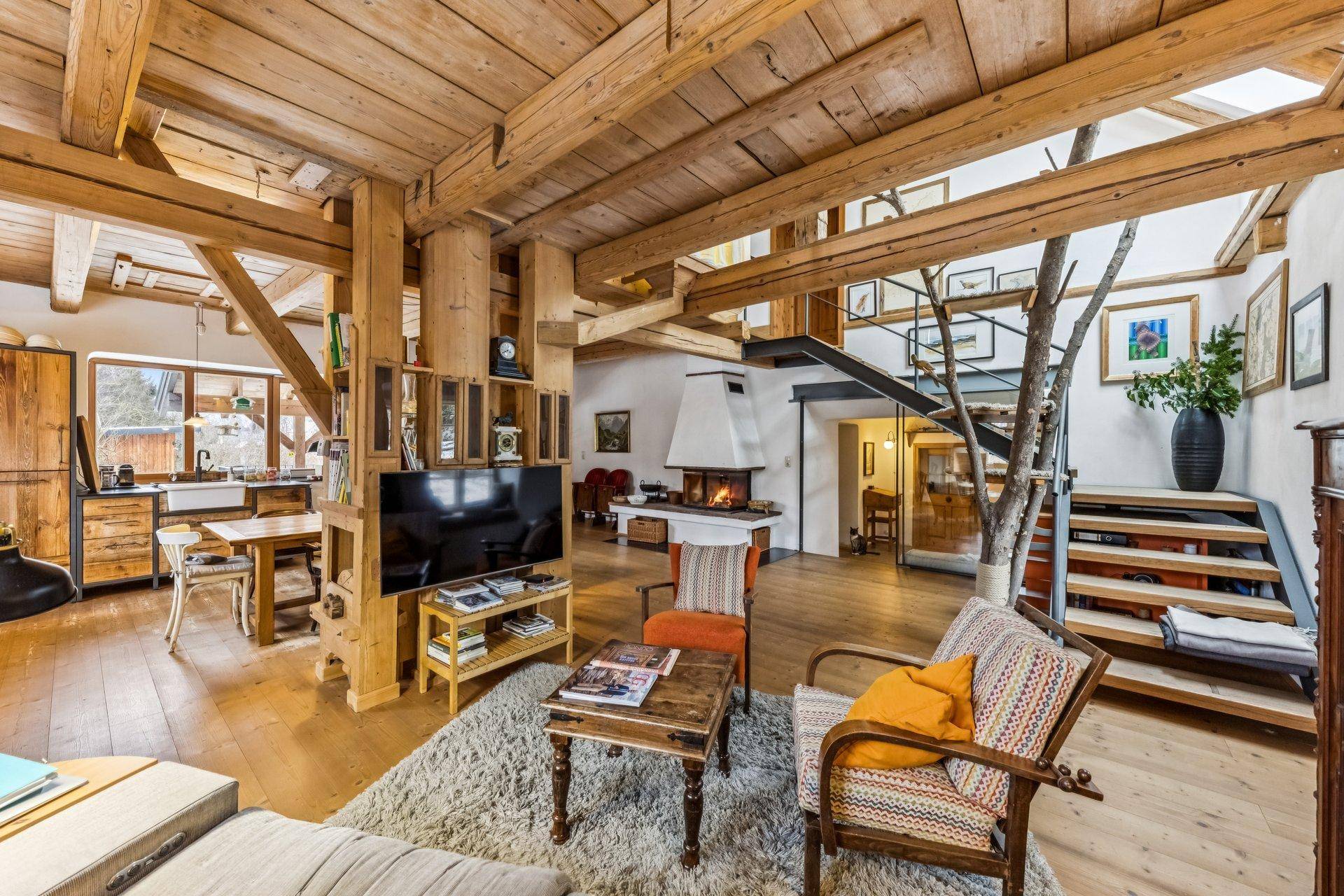 Geräumiges Wohnzimmer mit Holzbalken, Kamin und offener Treppe zum oberen Bereich.