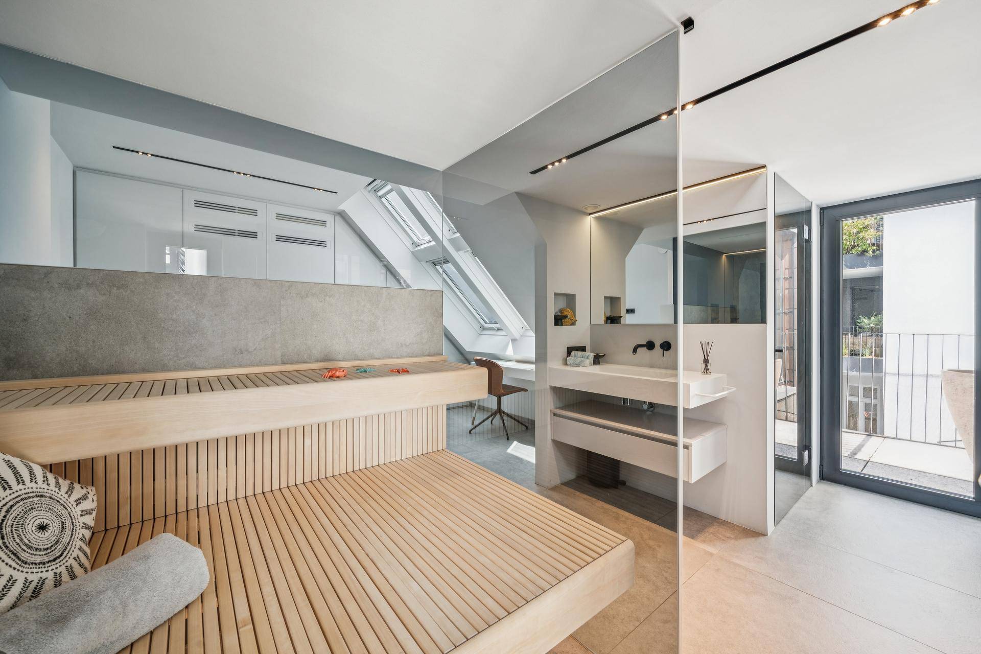 Wellnessbereich mit Sauna, modernem Waschtisch und Zugang zu einem kleinen Balkon.