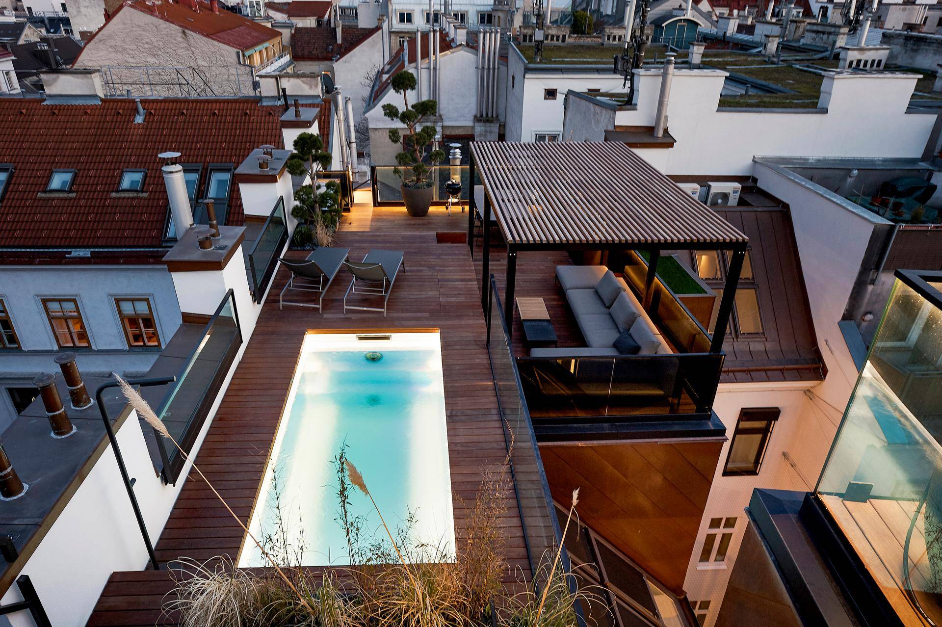 Dachterrasse mit Pool, Lounge-Bereich und weitem Blick über die Stadt bei Abenddämmerung.