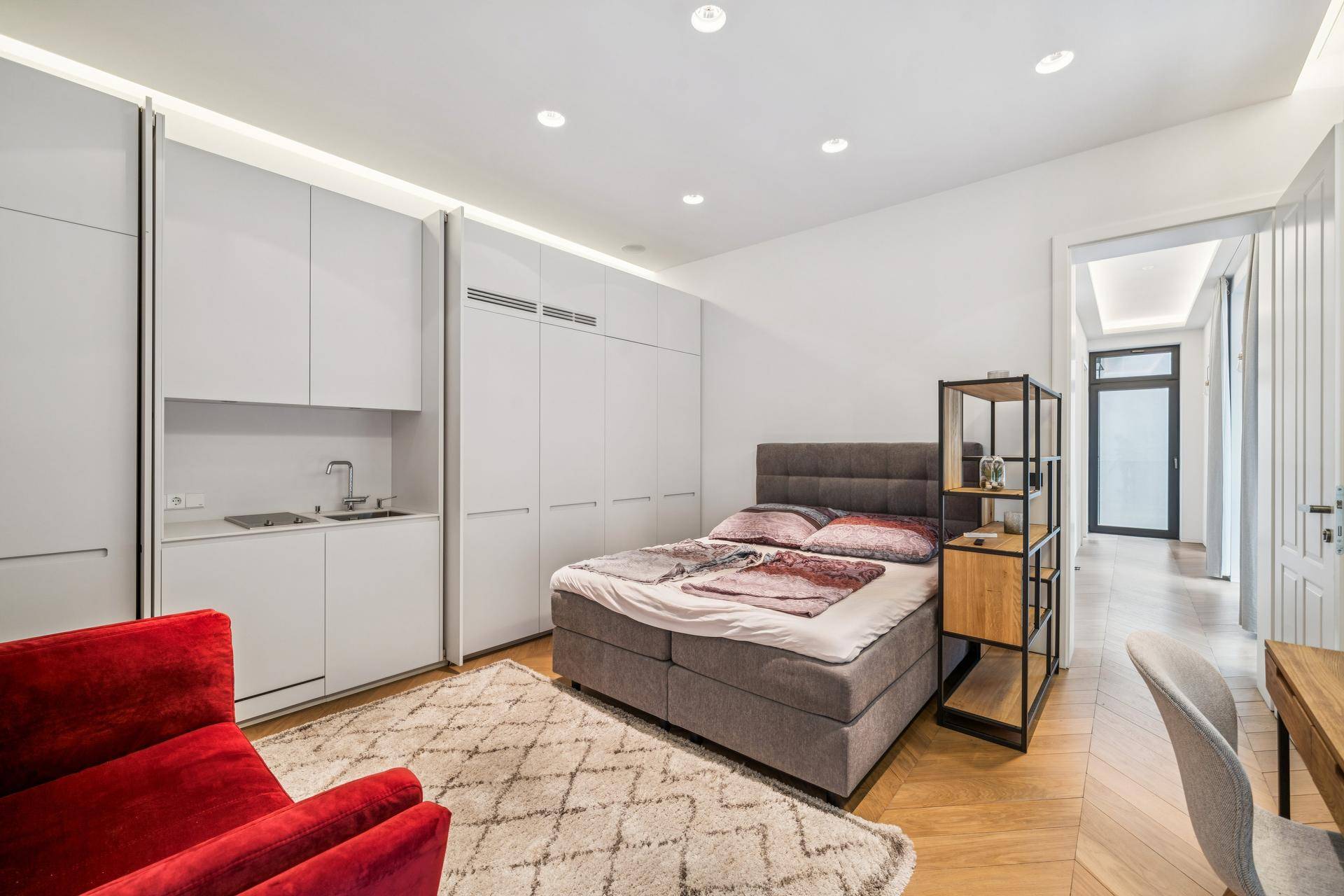 Schlafzimmer mit integrierter Küchenzeile, Einbauschränken und Parkettboden.