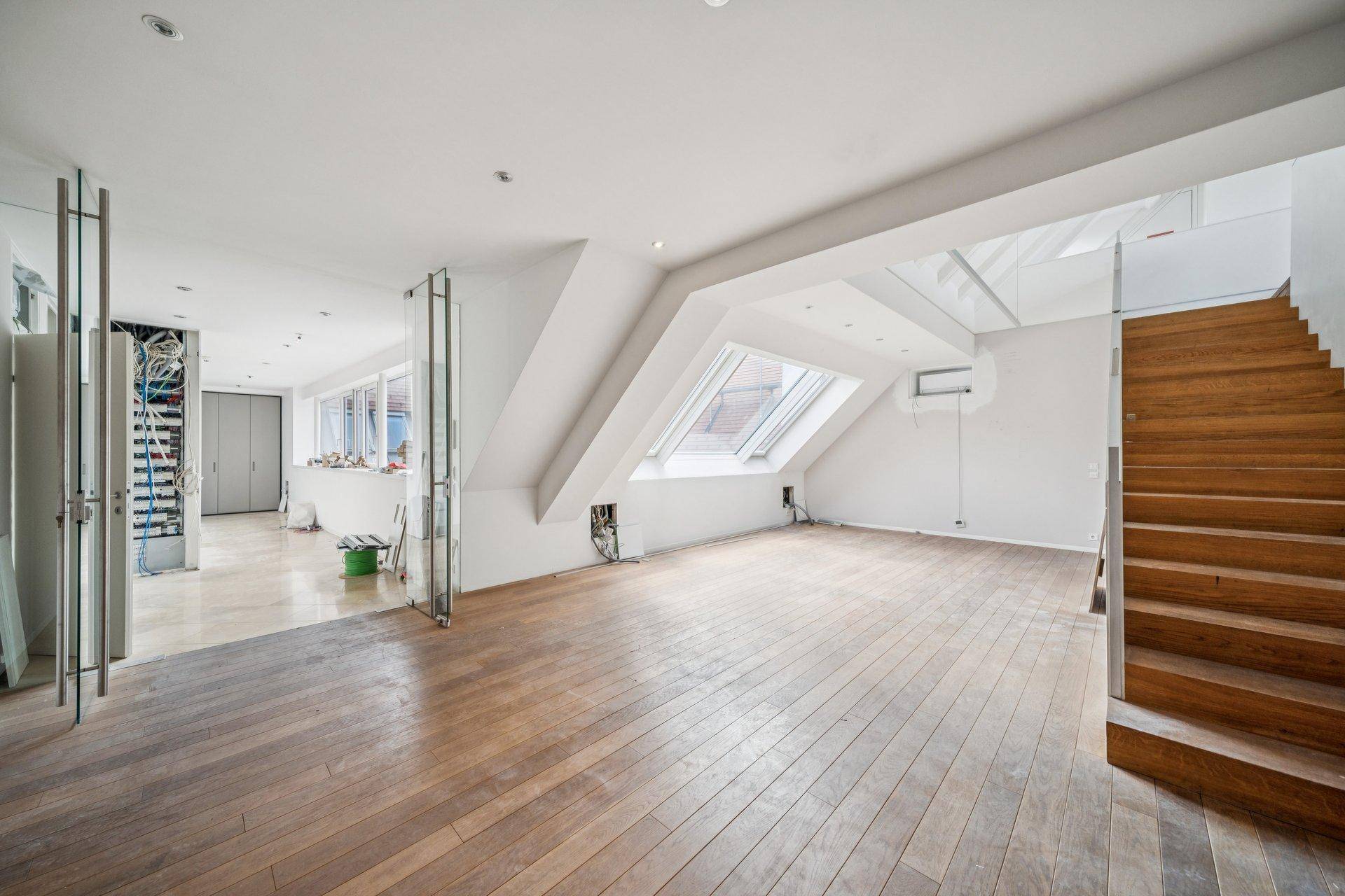 Heller, unmöblierter Wohnbereich im Dachgeschoss mit Holzboden und Treppe zu einer weiteren Ebene.