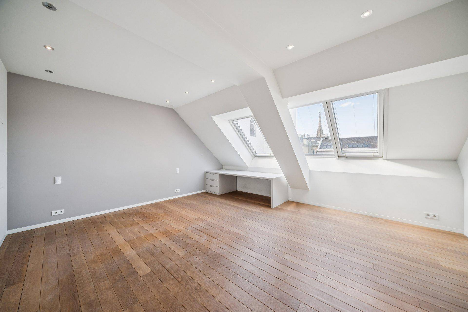 Leeres Schlafzimmer im Dachgeschoss mit Holzboden, Schrägfenstern und integriertem Schreibtisch.