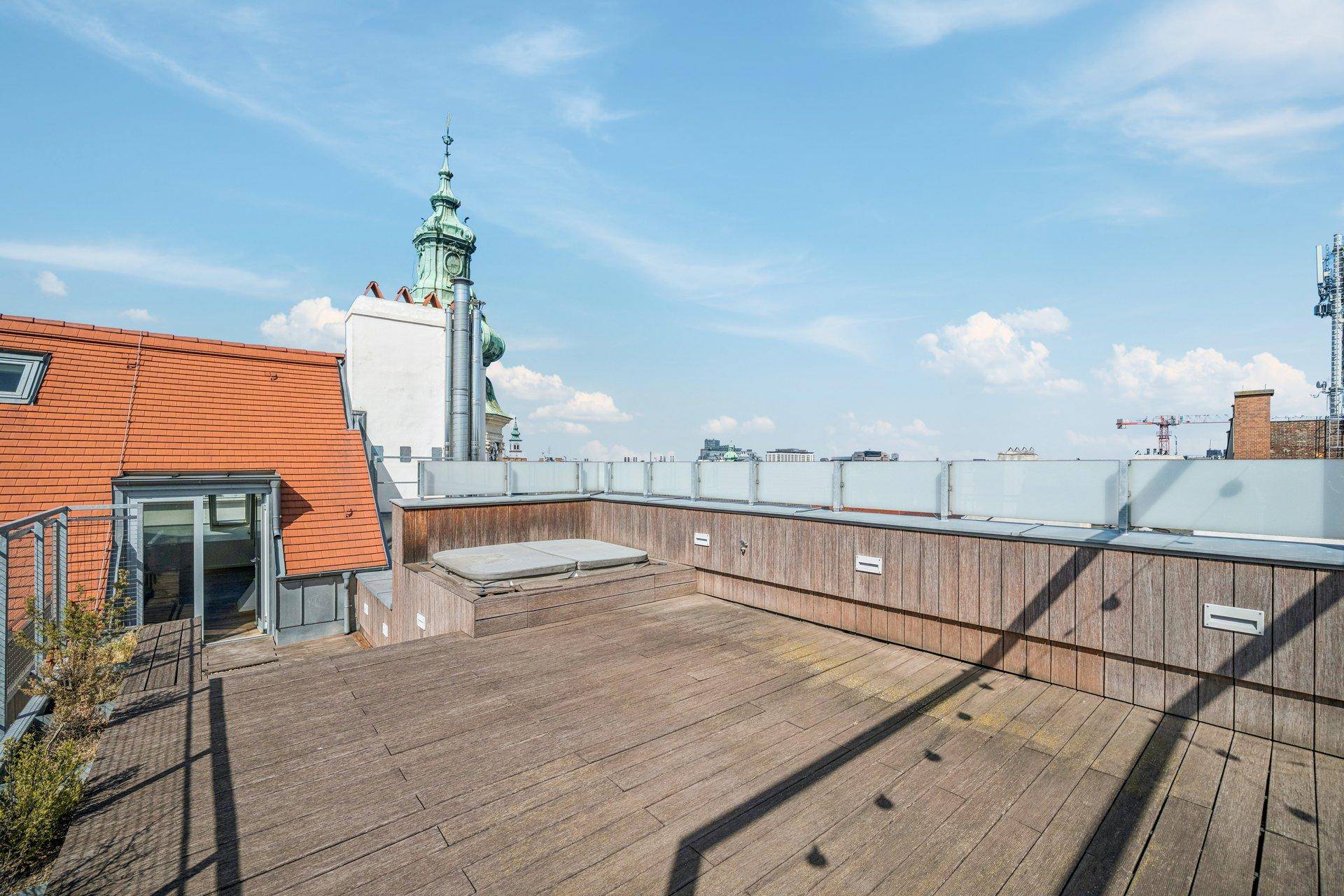 Weitläufige Dachterrasse mit Holzdeck, integriertem Whirlpool und historischem Kirchturm im Hintergrund.
