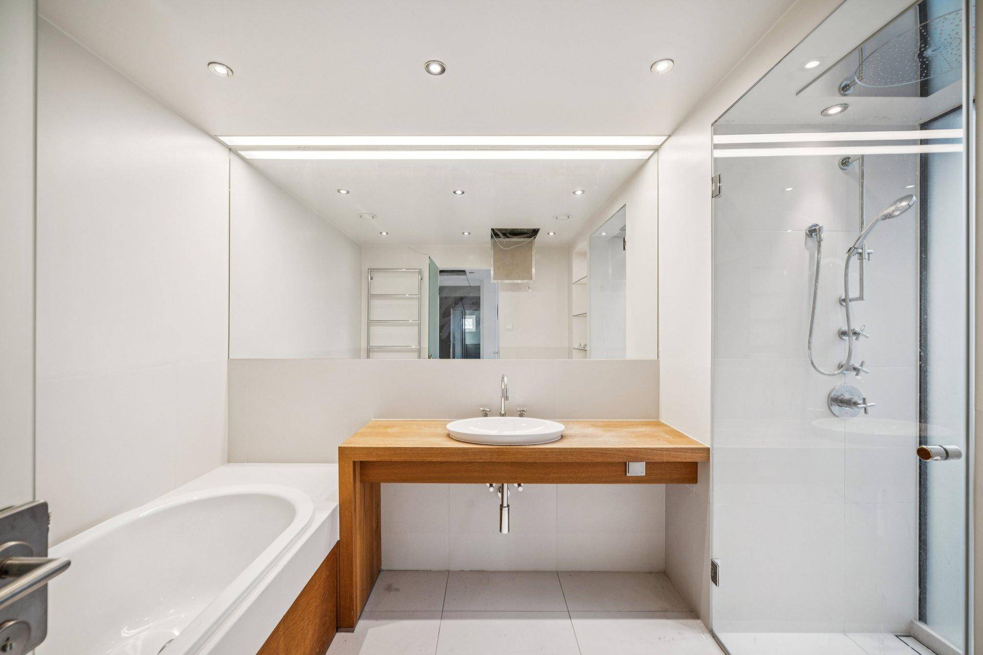 Modernes Badezimmer mit Badewanne, begehbarer Dusche und Holzwaschtisch unter großem Spiegel.