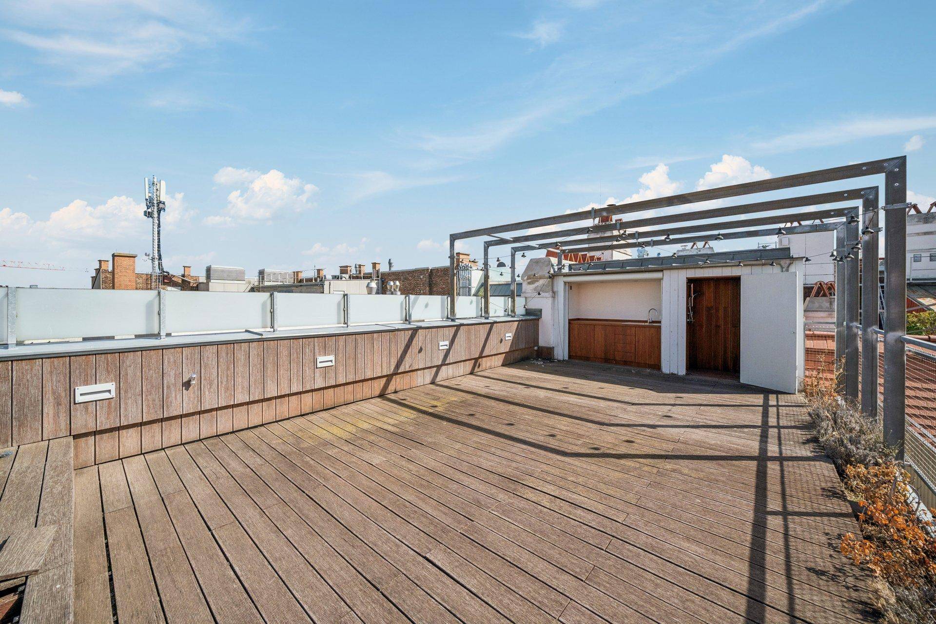 Große, unmöblierte Dachterrasse mit Holzdeck, Außenküche und Blick auf die Stadt.