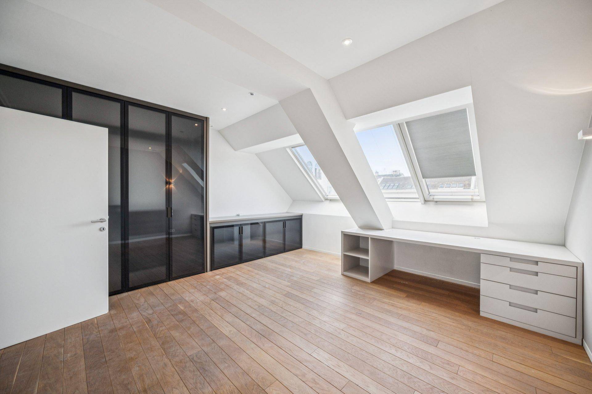 Unmöbliertes Arbeitszimmer im Dachgeschoss mit Holzboden, Schrägfenstern und Einbauschränken.
