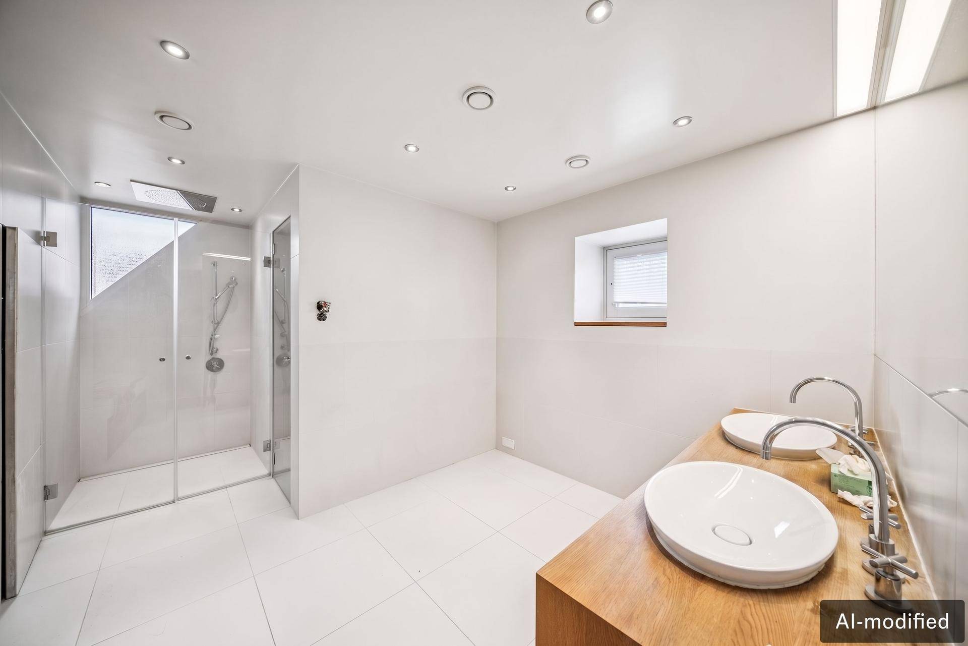 Helles Badezimmer mit zwei Waschbecken, begehbarer Dusche und kleinem Fenster.