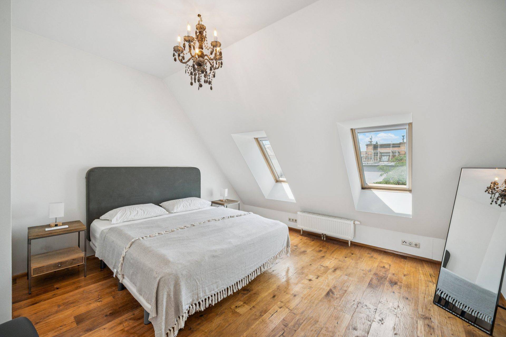 Gemütliches Schlafzimmer im Dachgeschoss mit Holzboden, Dachfenstern und einem eleganten Kronleuchter.