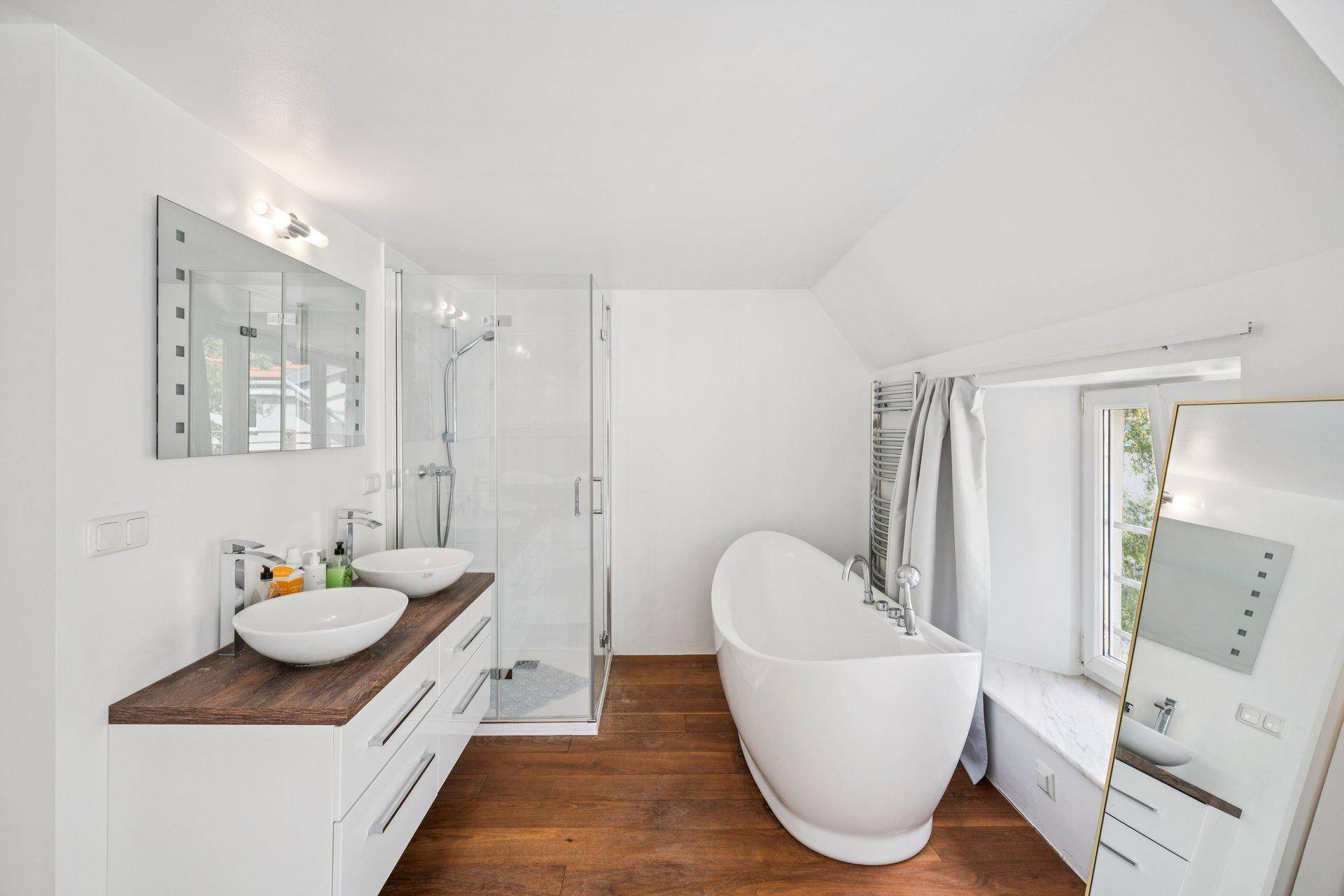 Modernes Badezimmer mit freistehender Badewanne, Doppelwaschbecken, Dusche und Holzboden.