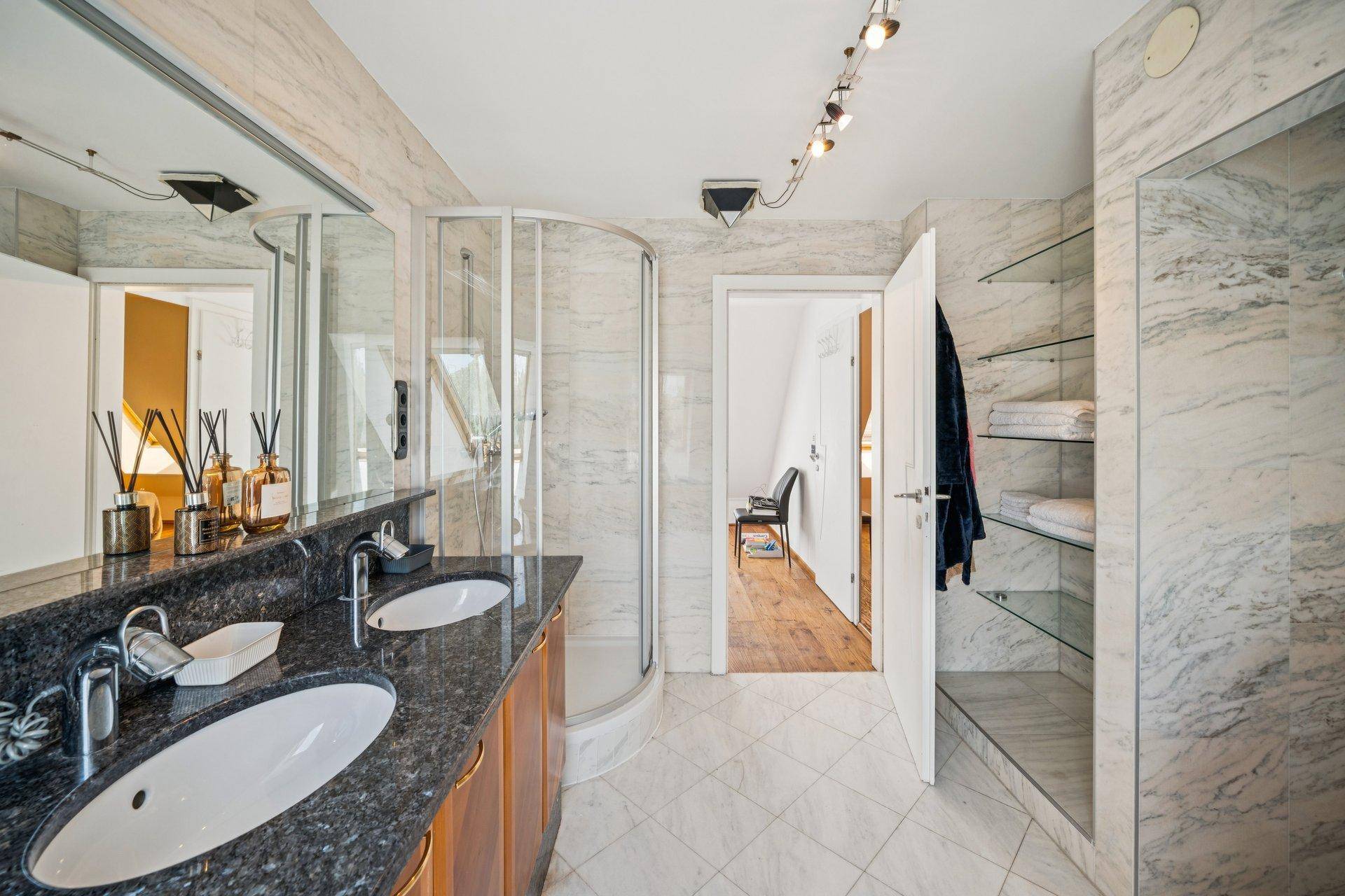 Elegantes Badezimmer mit Doppelwaschbecken, Dusche und Marmorfliesen an Wänden und Boden.