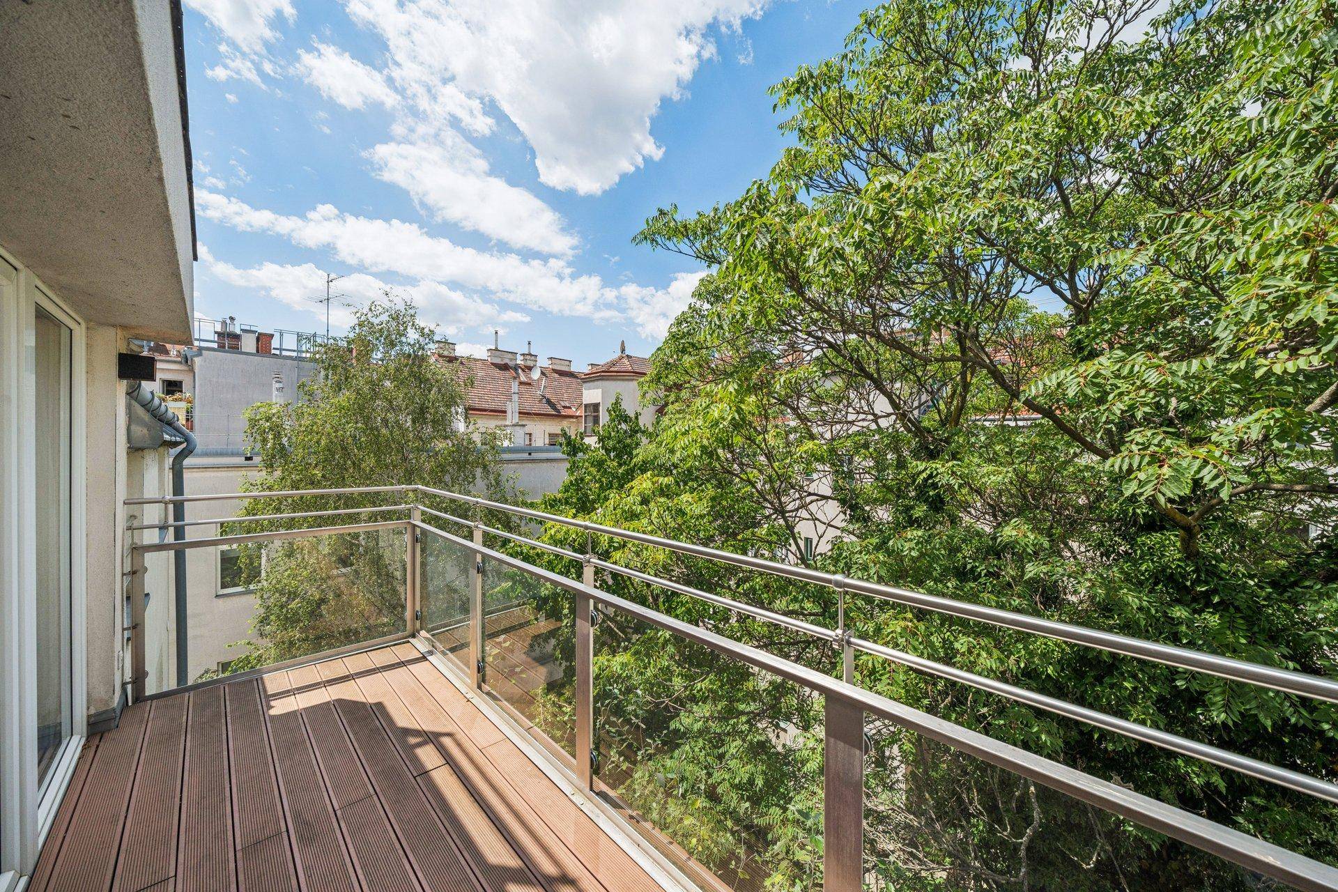Geräumiger Balkon mit Holzdeck, Glasgeländer und einem schönen Blick ins Grüne und auf die Stadt.