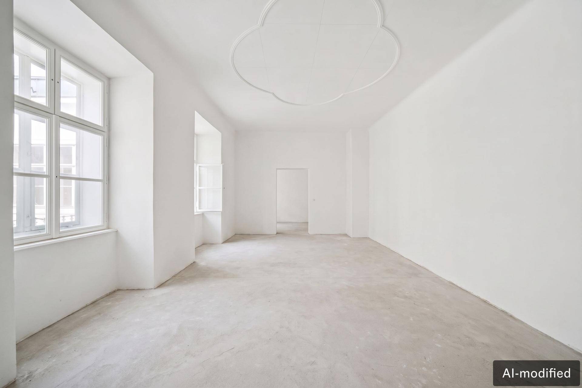 Geräumiger, heller Raum mit Betonboden, hohen Fenstern und dekorativer Stuckdecke.