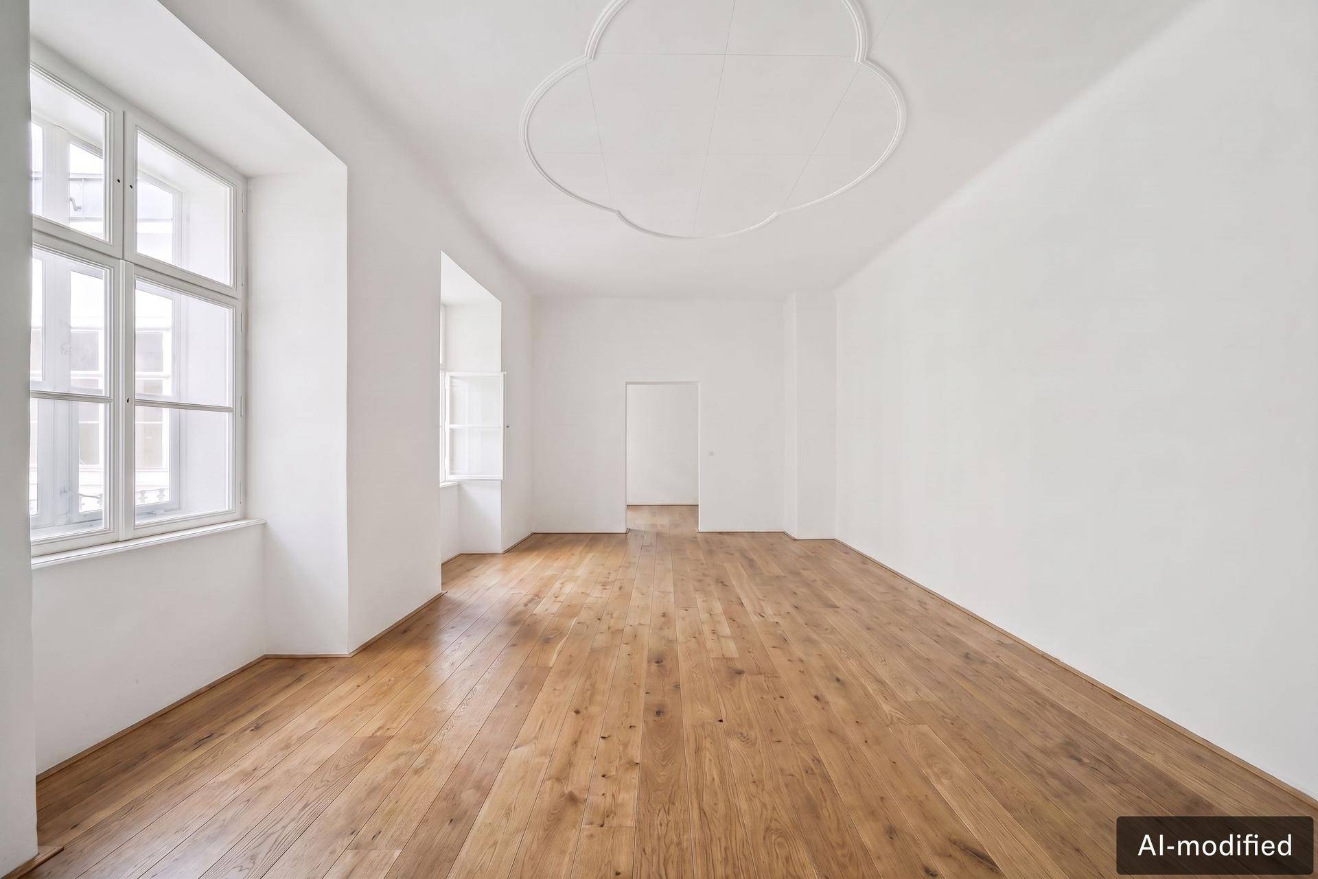 Geräumiger, heller Raum mit Holzdielenboden, hohen Fenstern und dekorativer Stuckdecke.