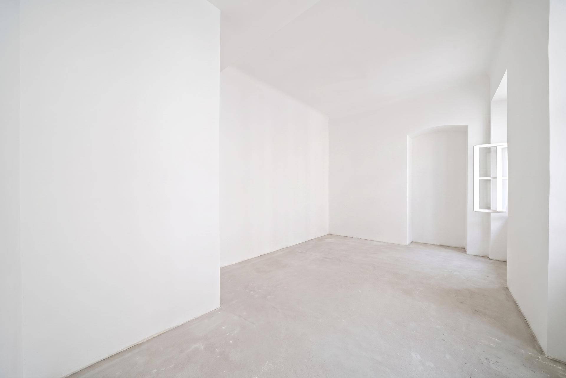 Heller Raum mit Betonboden und einem kleinen Fenster, geeignet als Schlaf- oder Arbeitszimmer.