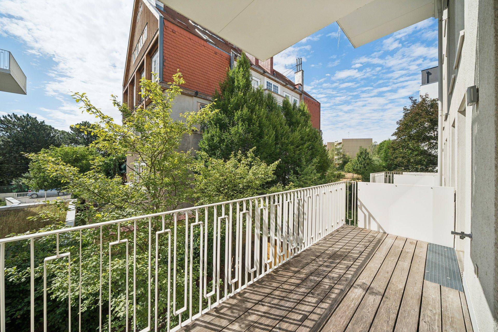 Heller Balkon mit Holzboden und Blick auf die umliegenden Gebäude und Bäume.