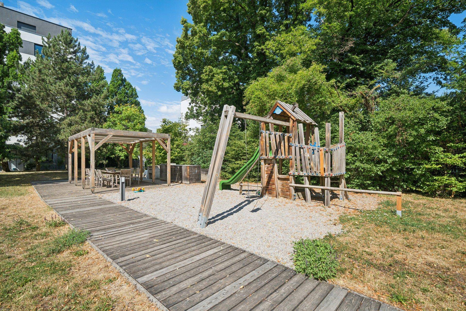 Gemeinschaftlicher Gartenbereich mit Kinderspielplatz, Schaukeln und Pergola für Entspannung.