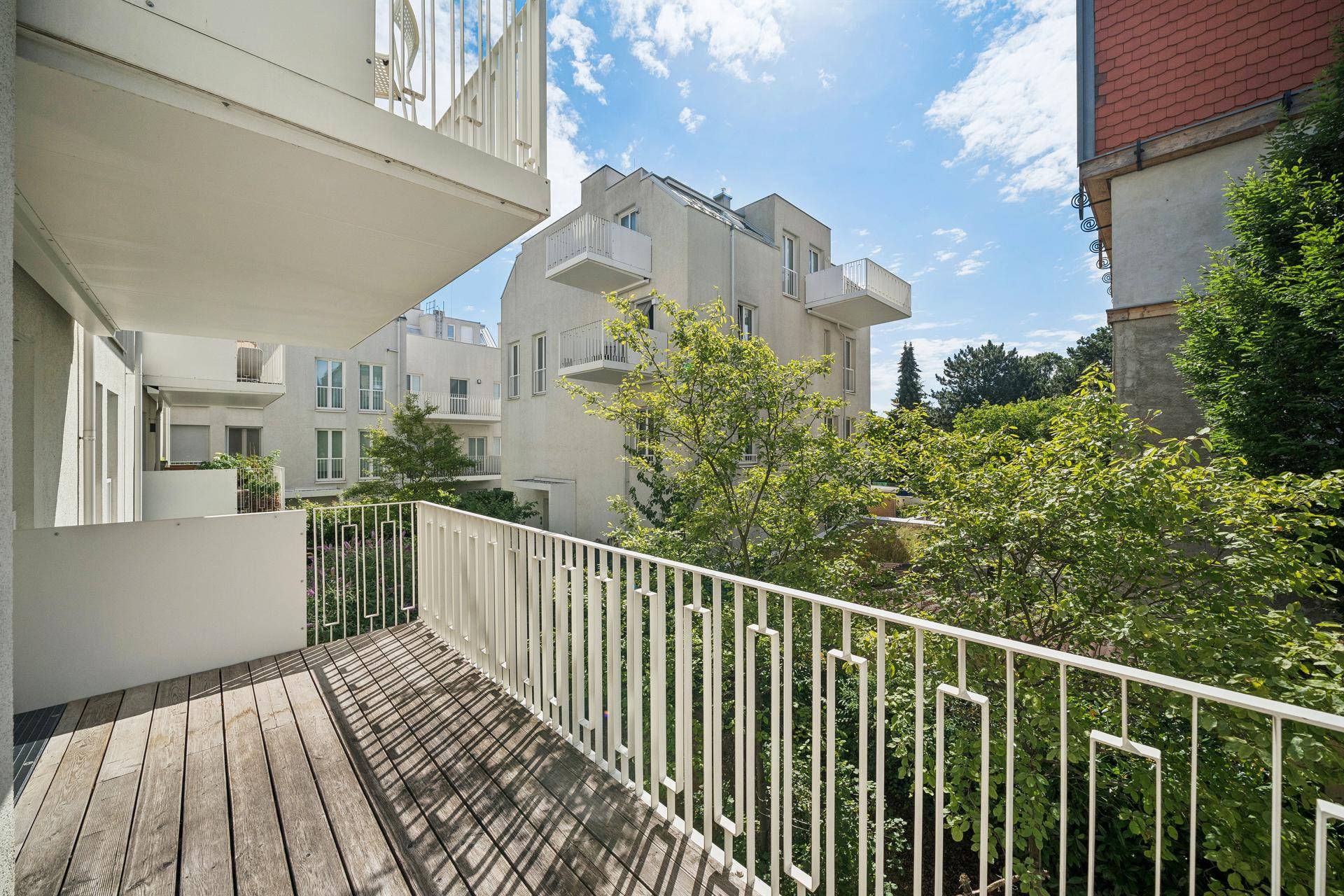 Geräumiger Balkon mit Holzboden und Blick auf die grüne Umgebung und moderne Gebäude.
