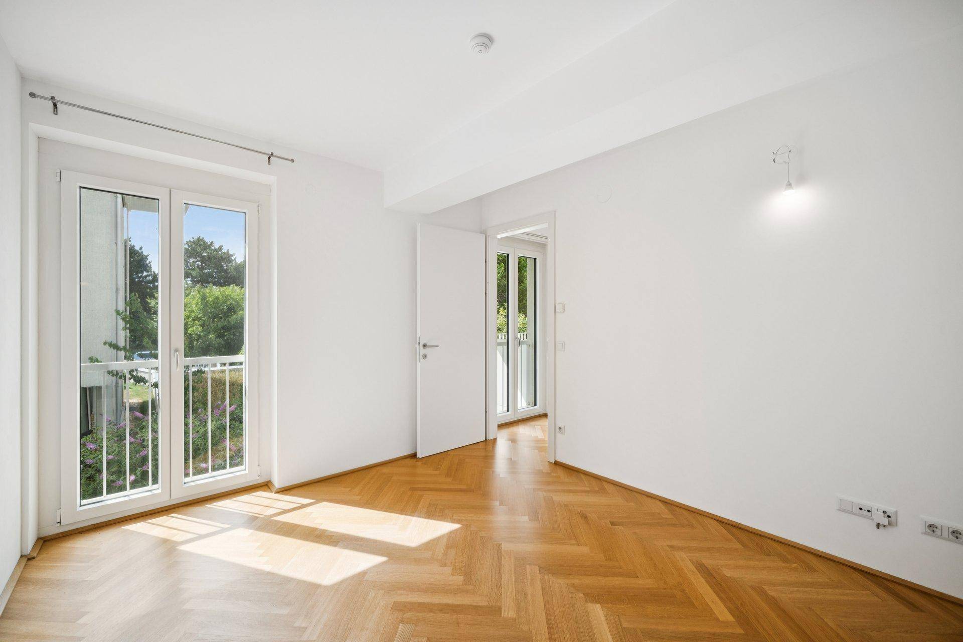 Lichtdurchflutetes Schlafzimmer mit Fischgrätparkett und Zugang zum Balkon.