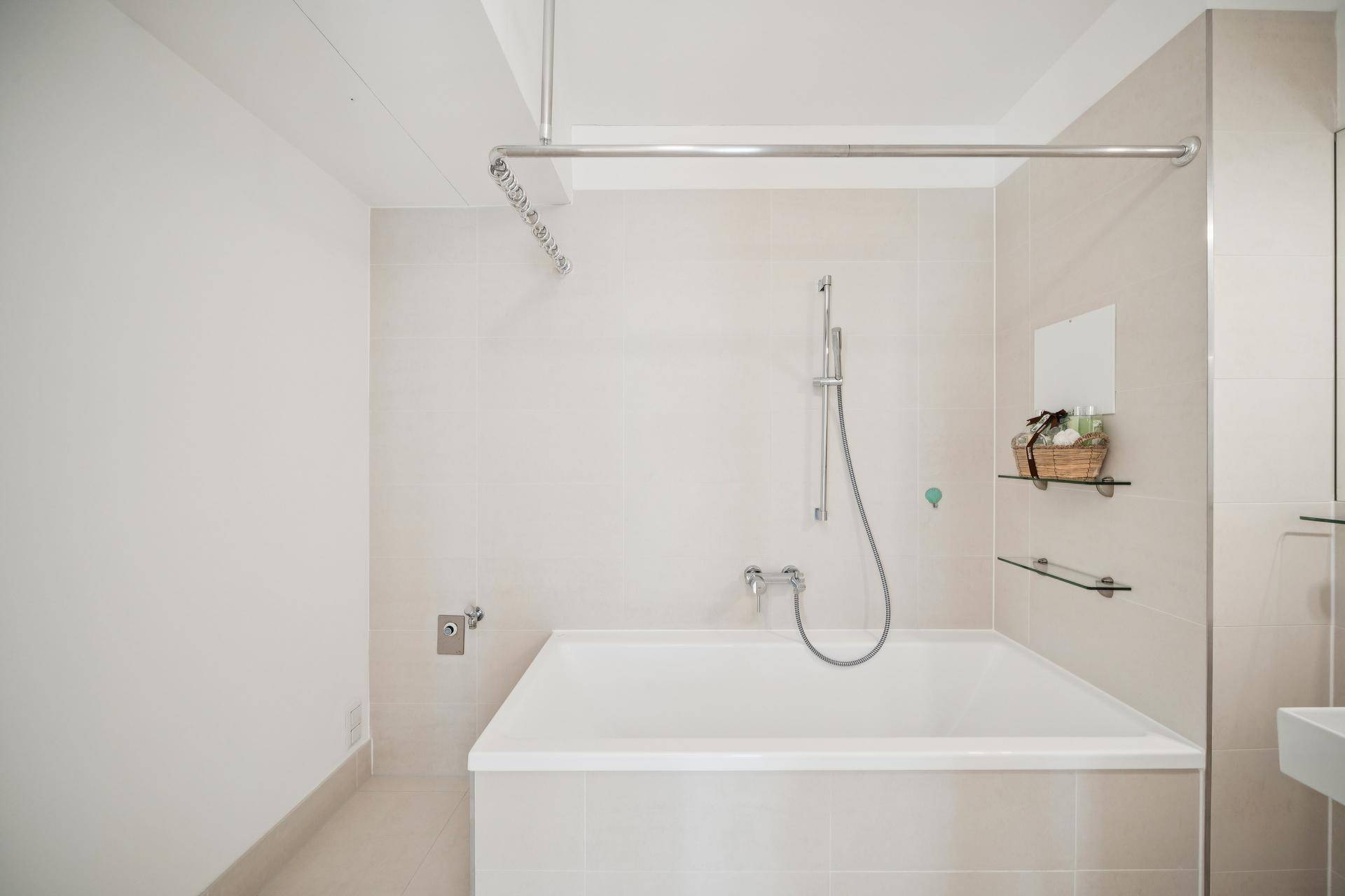 Modernes Badezimmer mit Badewanne, Duschvorhangstange und hellen Fliesen.
